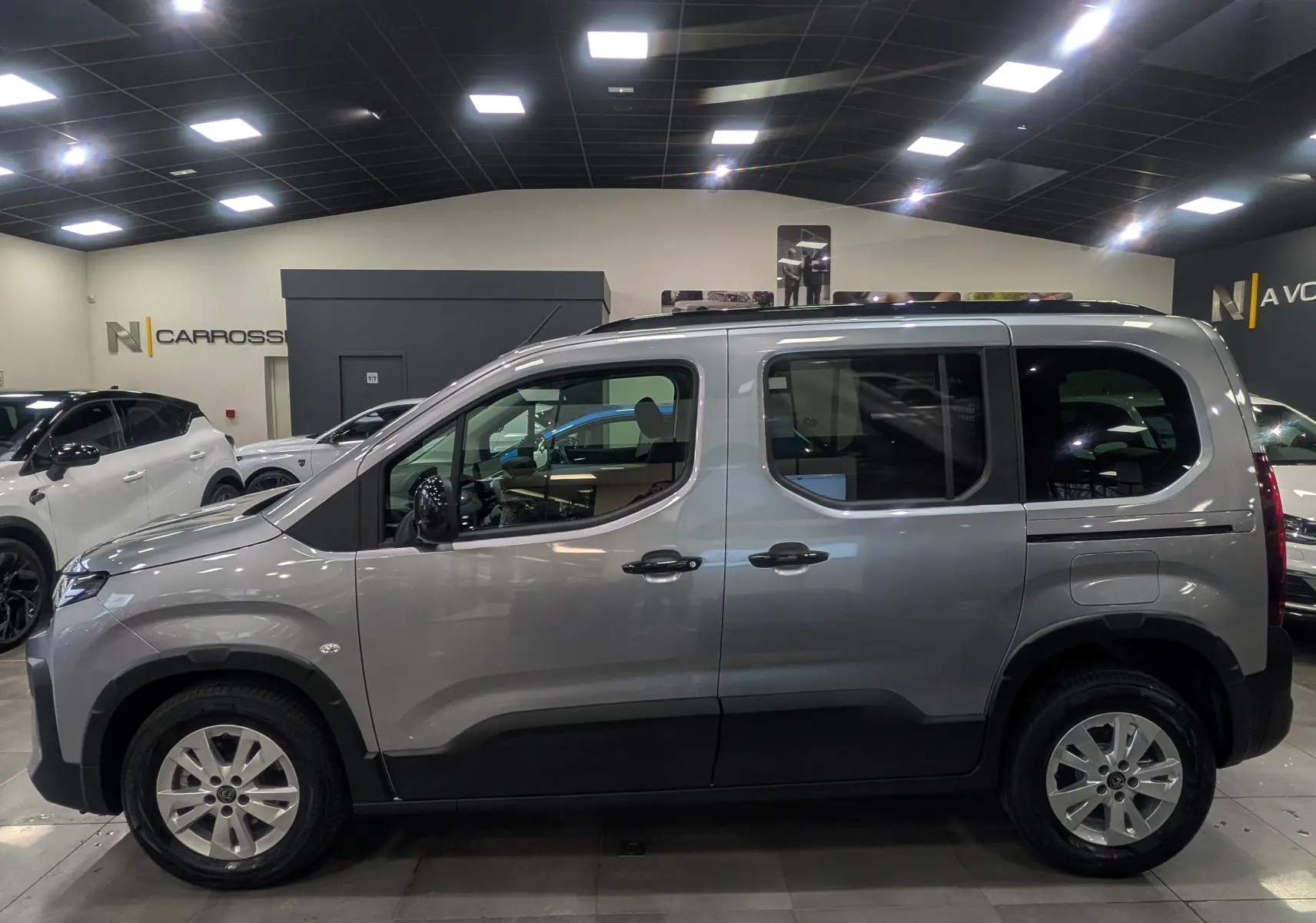 Vue de profil côté gauche d'un Peugeot Rifter gris acier 2025 en intérieur, avec jantes alliage et vitres teintées.