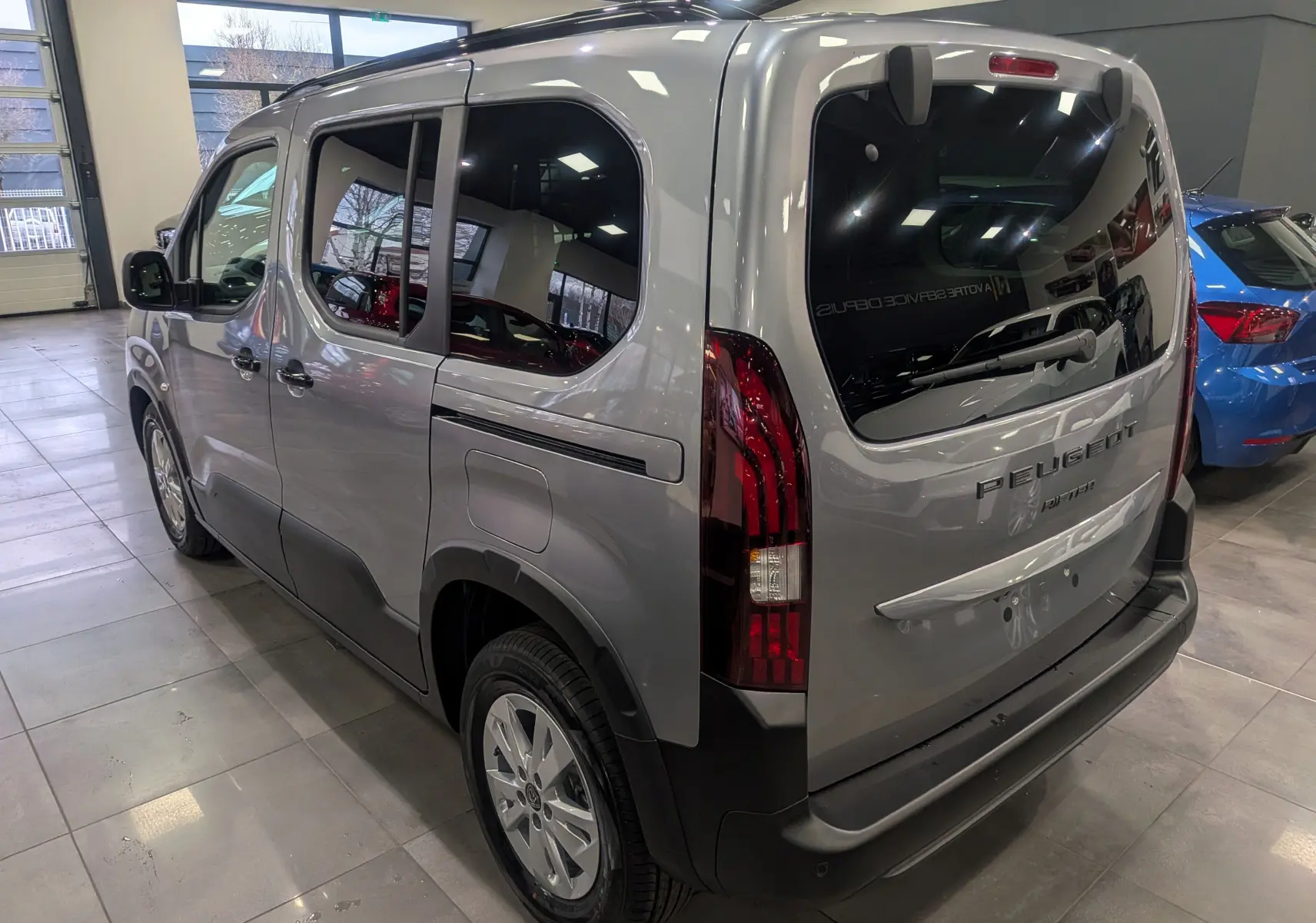 Vue 3/4 arrière droit du Peugeot Rifter gris acier 2025, avec vitres teintées et feux arrière verticaux distinctifs.