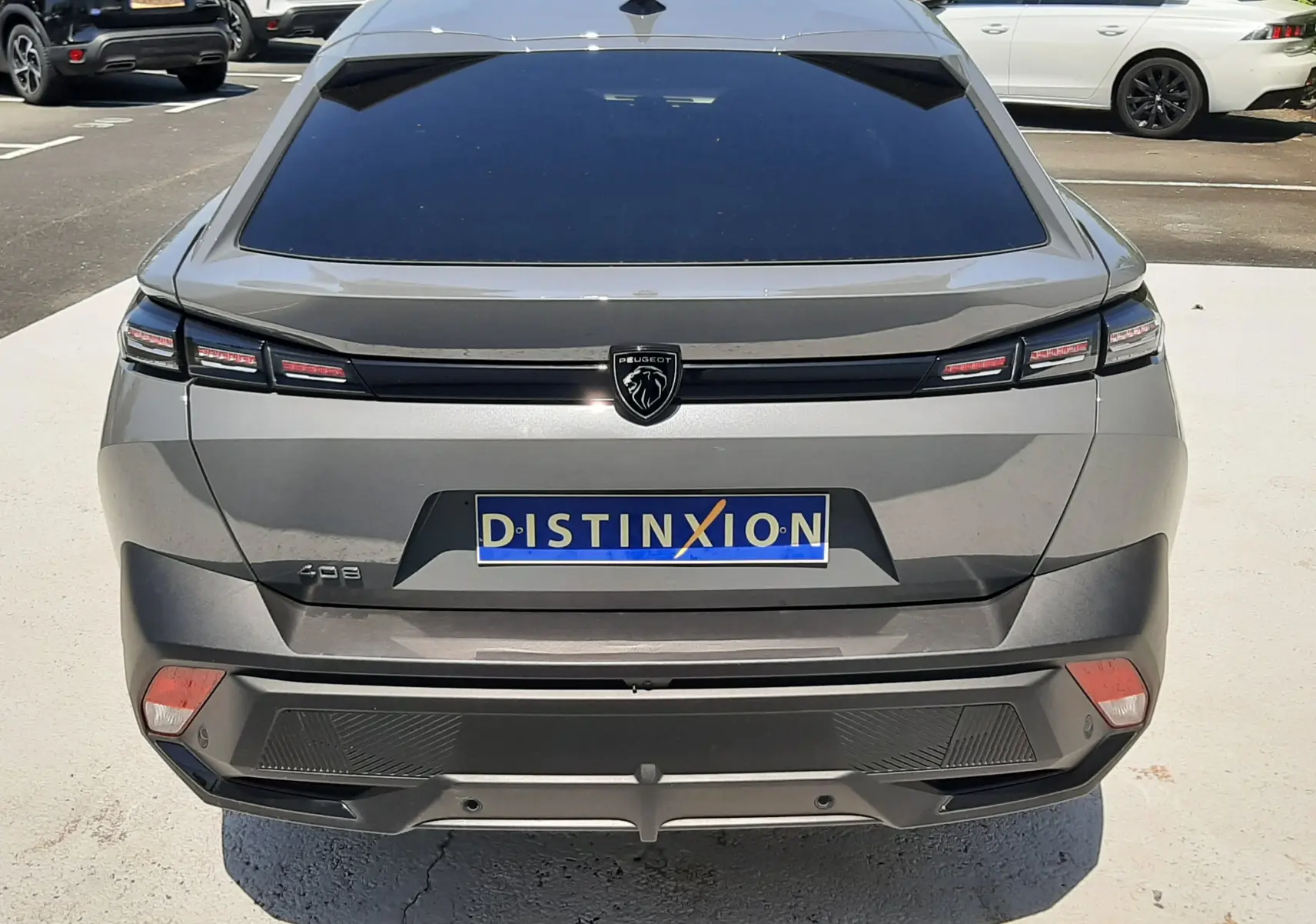 Vue arrière d'une Peugeot 408 HYBRID gris selenium 2024 avec feux LED étirés et logo lion central noir.