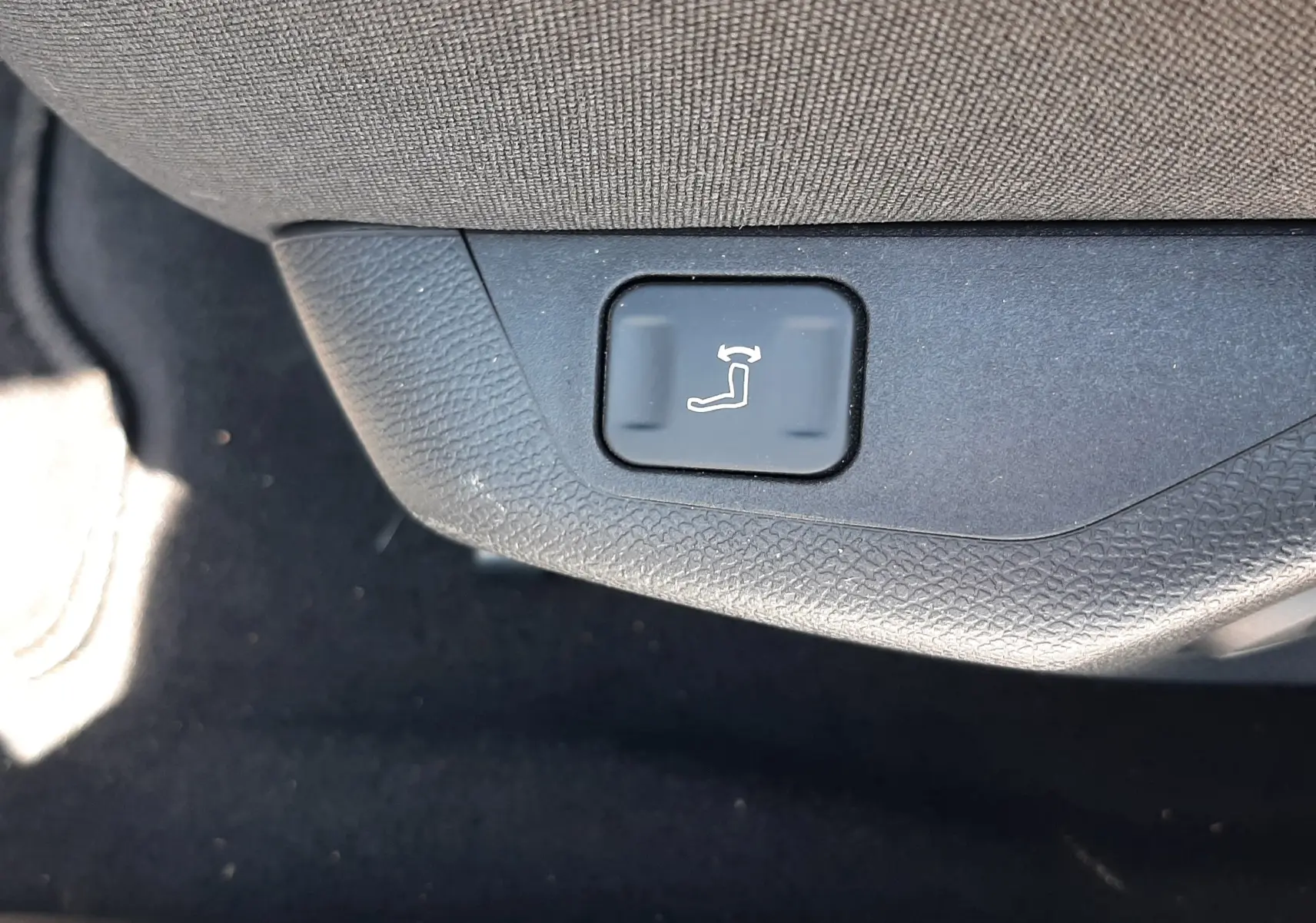 Gros plan sur le bouton de réglage électrique de l'inclinaison du siège côté conducteur dans un Peugeot 408 gris.