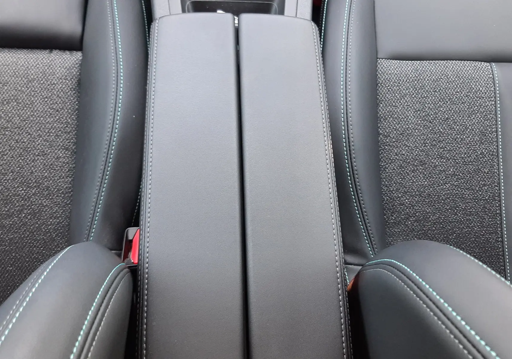 Vue plongeante sur l'accoudoir central en cuir noir avec surpiqûres bleues et sièges tissu et cuir gris du Peugeot 408 2024.