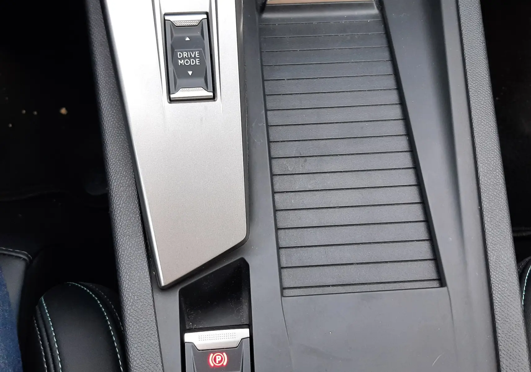 Vue rapprochée de la console centrale noire et grise du Peugeot 408 Hybrid 2024 avec bouton Drive Mode et frein à main électronique.