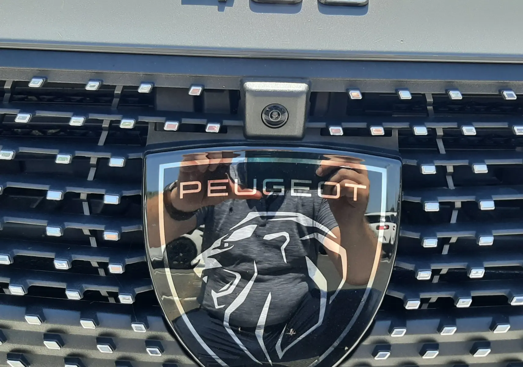 Gros plan sur la calandre gris sélénium du Peugeot 408 2024 avec logo lion et caméra frontale intégrée.