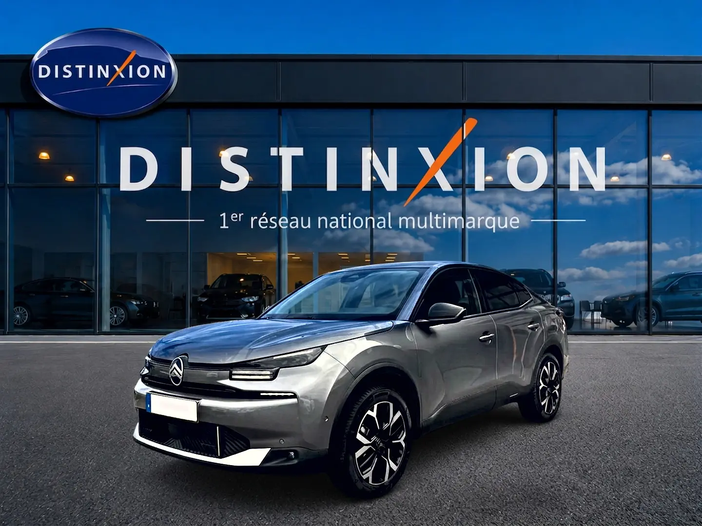 Citroën C4 X gris mercure en 3/4 avant droit, avec jantes alu et calandre distinctive, devant un showroom Distinxion.