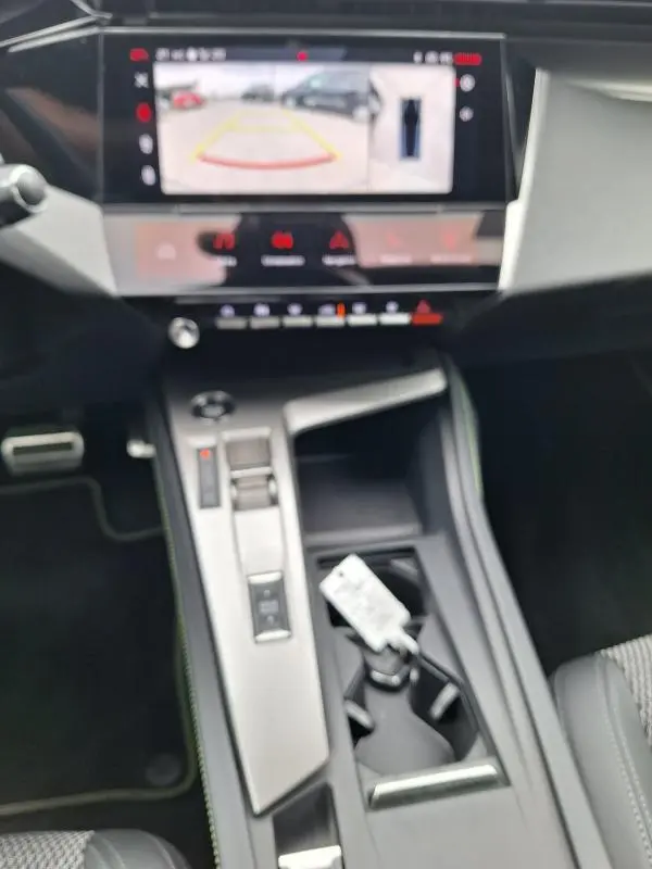 Vue intérieure centrée sur la console centrale et l'écran tactile affichant la caméra de recul du Peugeot 308 gris Hybrid 145 e-DCS6 GT.