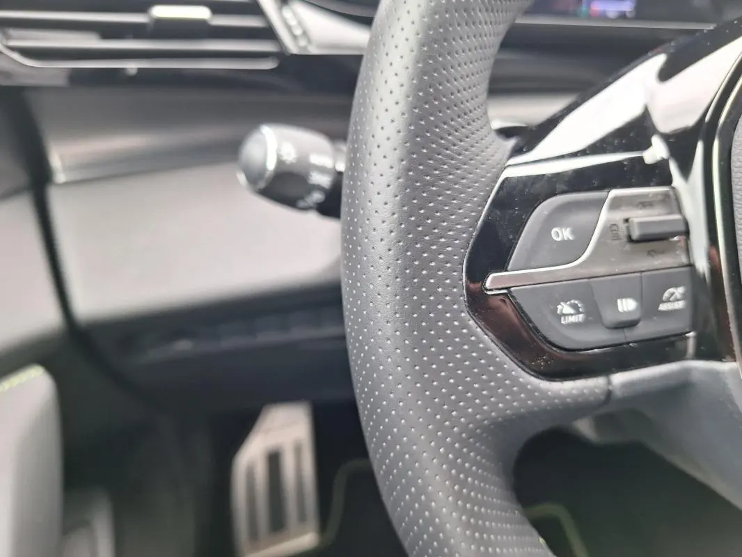 Gros plan sur le volant perforé et les commandes multifonctions du Peugeot 308 Hybrid 145 e-DCS6 GT, intérieur noir.