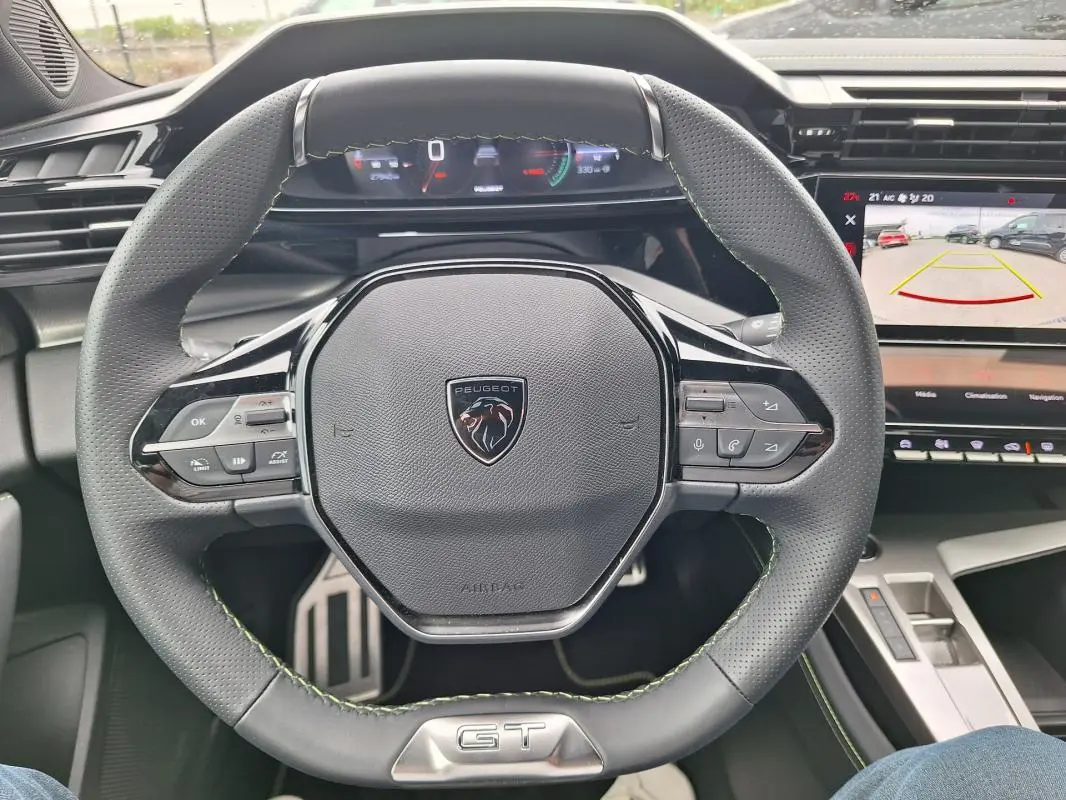 Vue intérieure centrée sur le volant gris perforé du Peugeot 308 Hybrid 145 e-DCS6 GT avec cockpit numérique et écran multimédia.