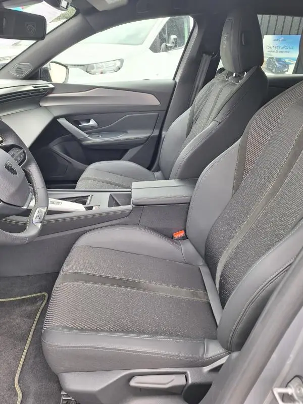 Vue intérieure côté conducteur de la Peugeot 308 Hybrid 145 e-DCS6 GT 2025 gris, sièges tissu et cuir, tableau de bord moderne.