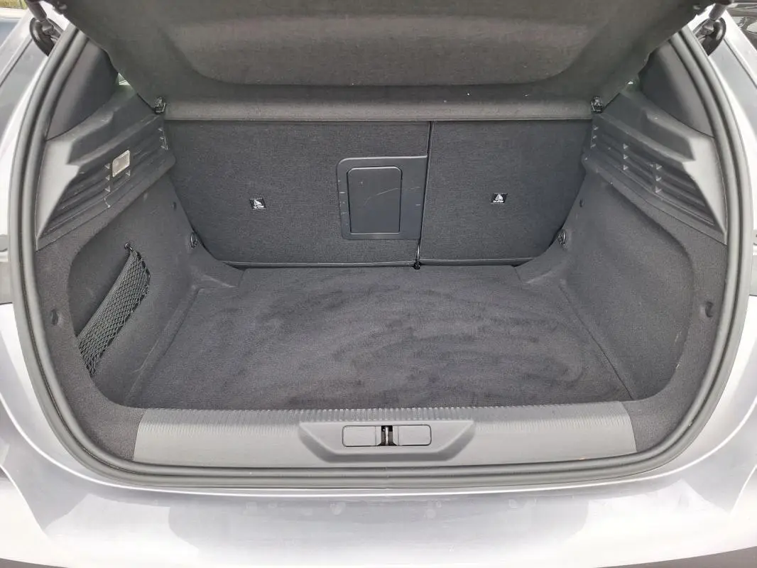 Coffre ouvert vu de l'arrière d'une Peugeot 308 Hybrid 145 gris, montrant un espace de rangement propre et spacieux.