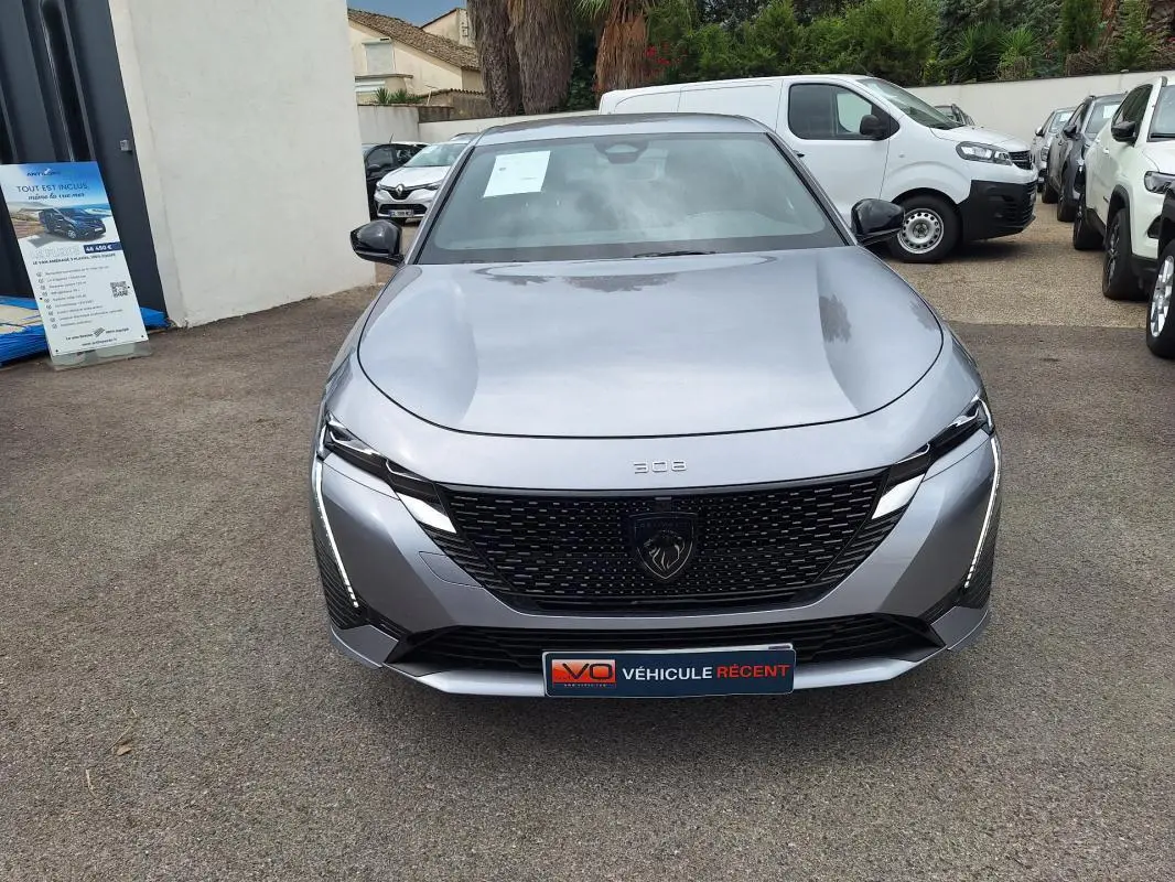 Vue avant d'une Peugeot 308 Hybrid 145 e-DCS6 GT gris métallisé avec calandre noire et feux LED fins.