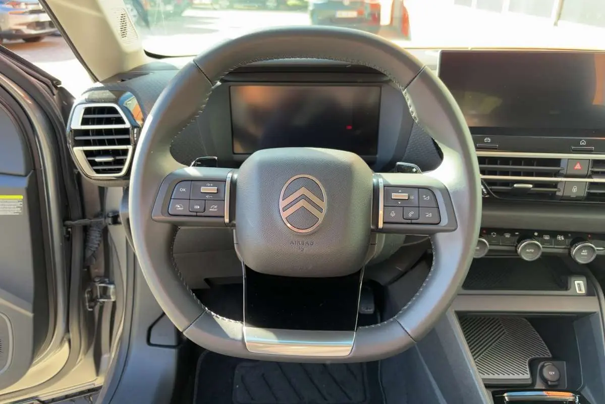 Vue centrée sur le volant cuir et tableau de bord numérique du Citroën C4 hybride 2025, intérieur gris.