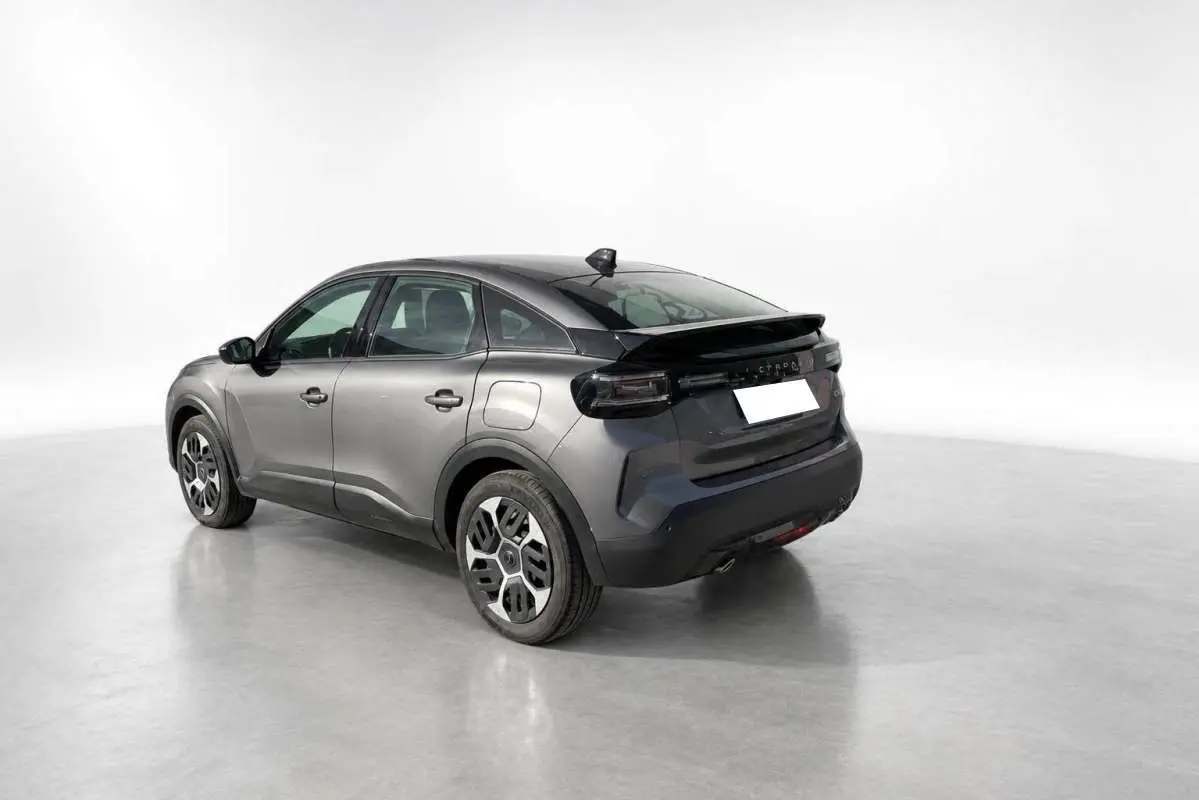 Vue 3/4 arrière droite d'une Citroën C4 hybride 2025 gris mercury avec jantes acier 18 pouces et feux arrière foncés.