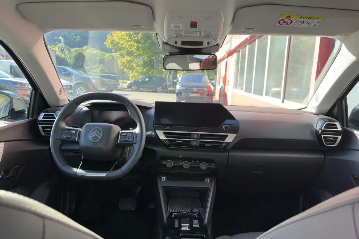 Vue intérieure avant du Citroën C4 hybride 2025, tableau de bord noir avec volant cuir et écran tactile central.