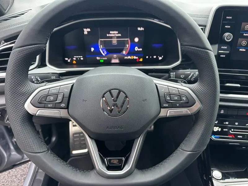 Vue rapprochée du volant en cuir perforé du Volkswagen T-Roc gris 2025, avec commandes intégrées et tableau de bord numérique.