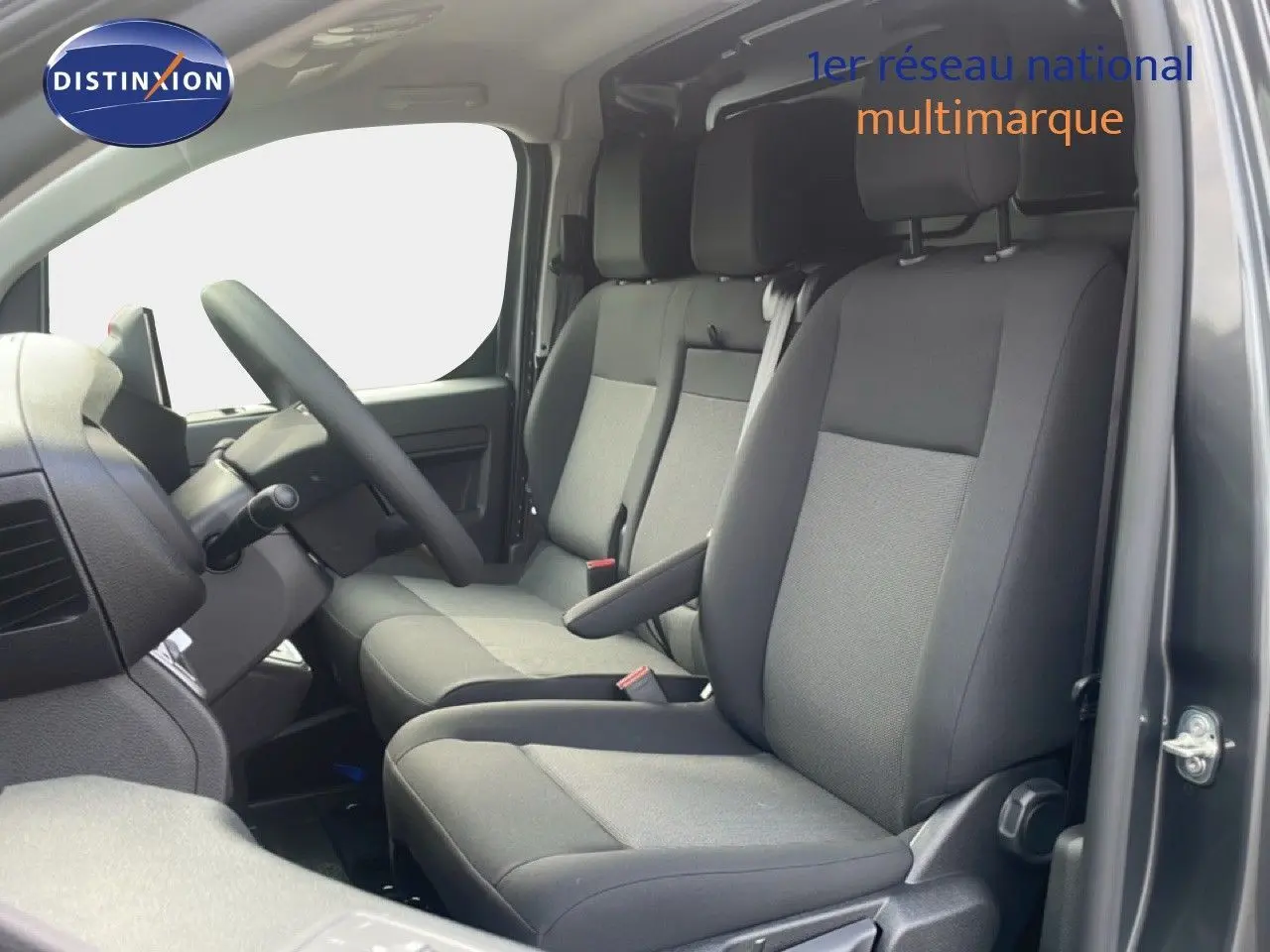 Vue intérieure côté conducteur du Citroën Jumpy gris titane, montrant les sièges tissu gris et le volant multifonction.