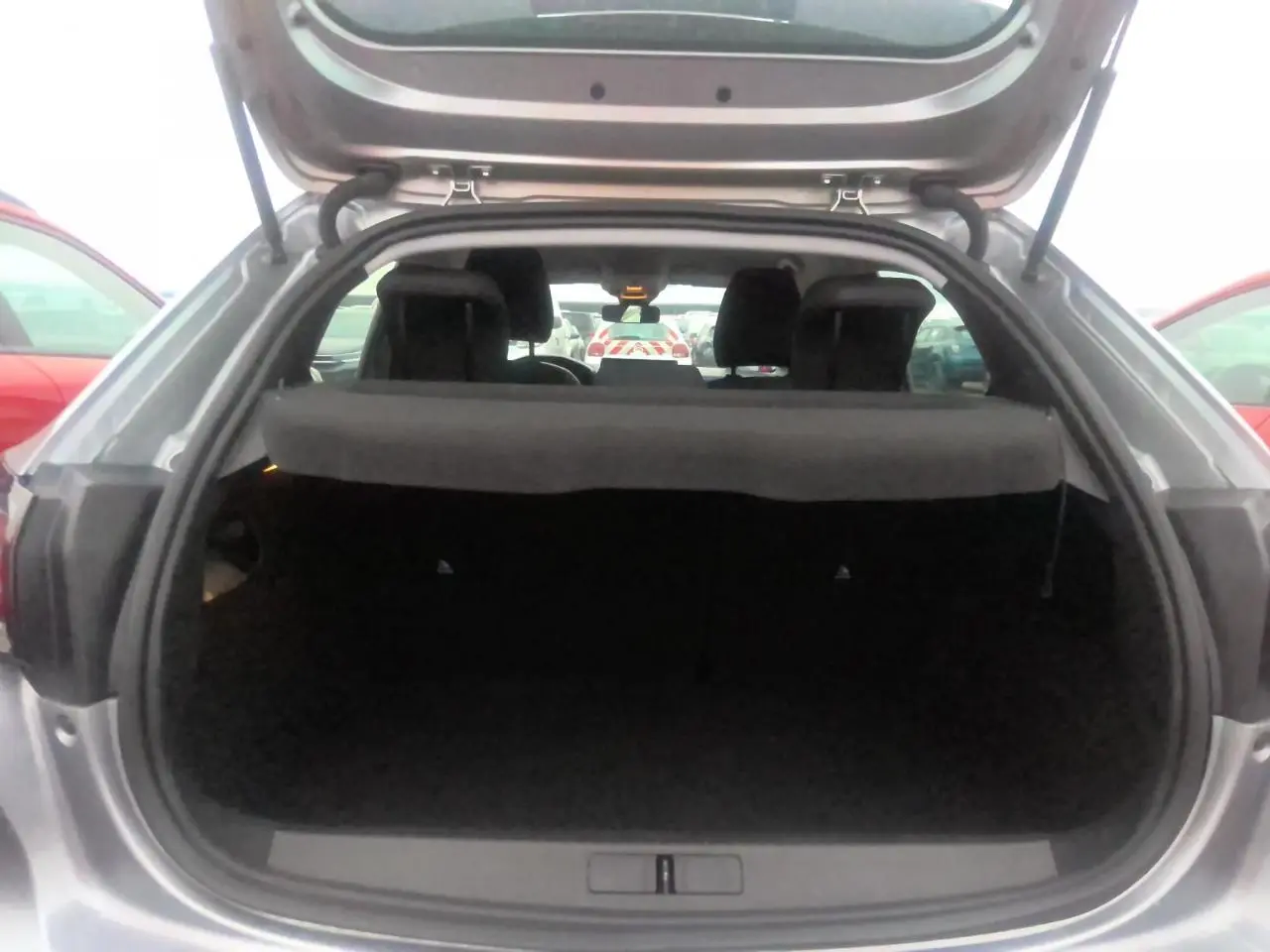 Coffre ouvert vu de l'arrière d'une Peugeot 208 gris clair 2024, montrant l'espace de chargement vide.