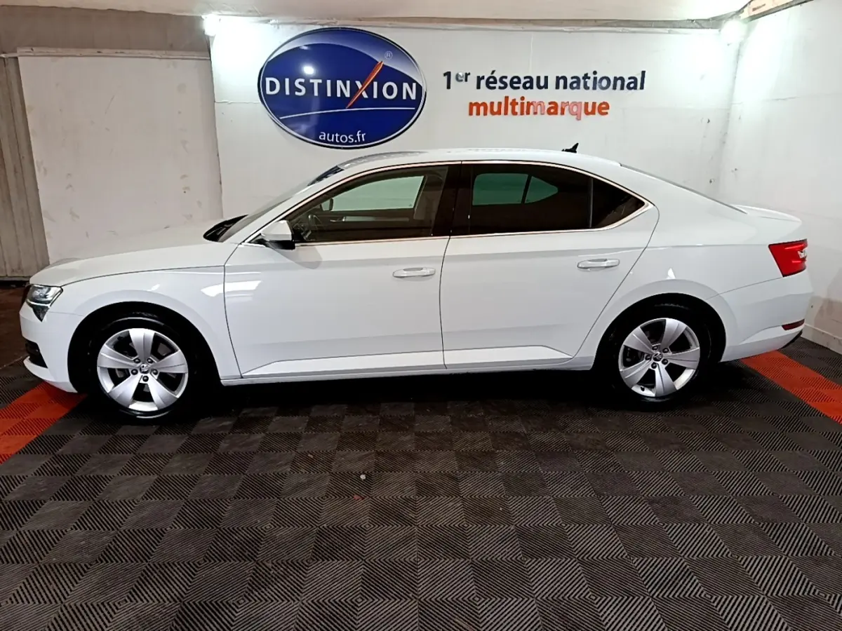 Vue de profil côté gauche d'une Skoda Superb blanche de 2021, berline élégante avec jantes alliage et vitres teintées.