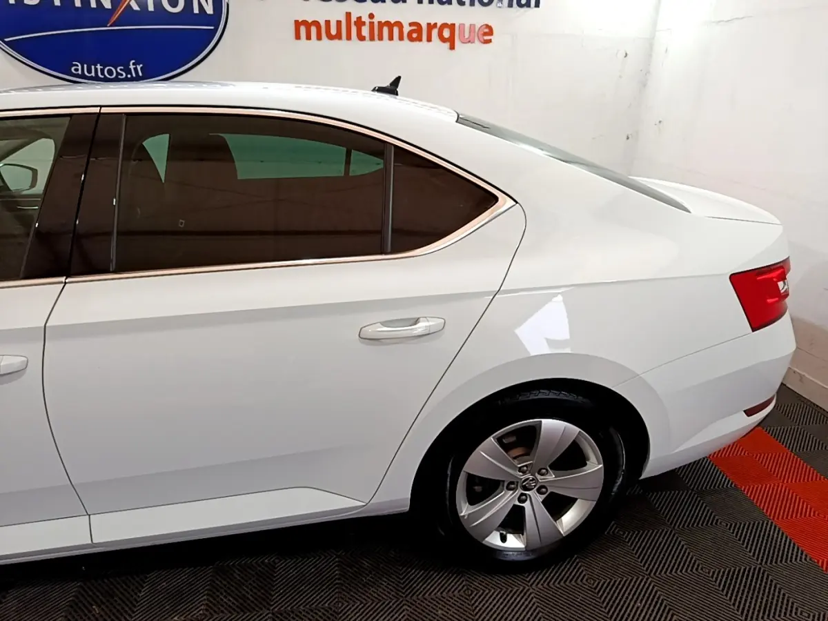 Vue latérale droite d’une Skoda Superb blanche 2021 avec jantes alliage et vitres teintées en intérieur showroom.
