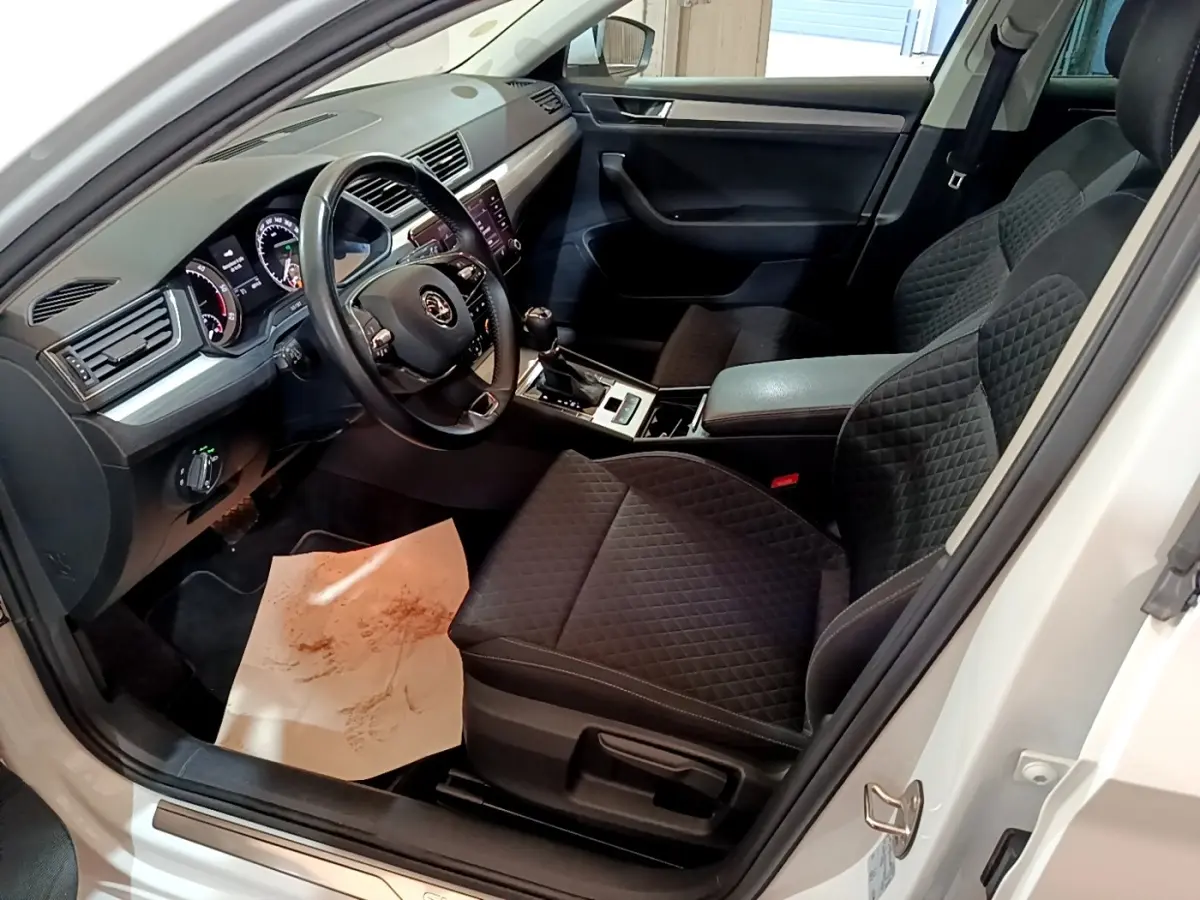 Intérieur côté conducteur d'une Skoda Superb blanc 2021, sièges noirs matelassés et tableau de bord moderne.