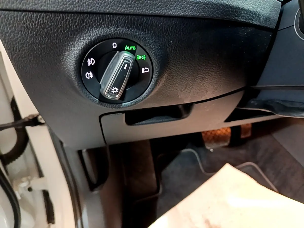 Gros plan sur le bouton de commande des phares en position automatique, tableau de bord noir d'une Skoda Superb blanche.
