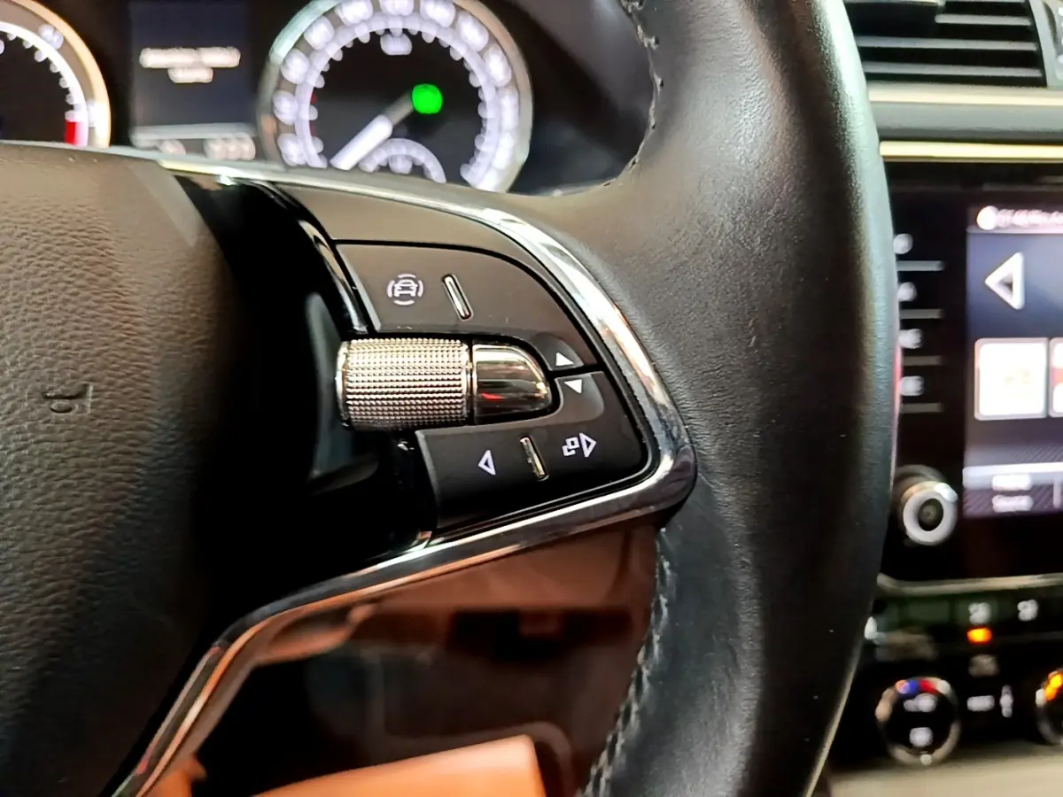 Gros plan sur les commandes gauche du volant cuir noir de la Skoda Superb 2021, avec tableau de bord et écran tactile en arrière-plan.