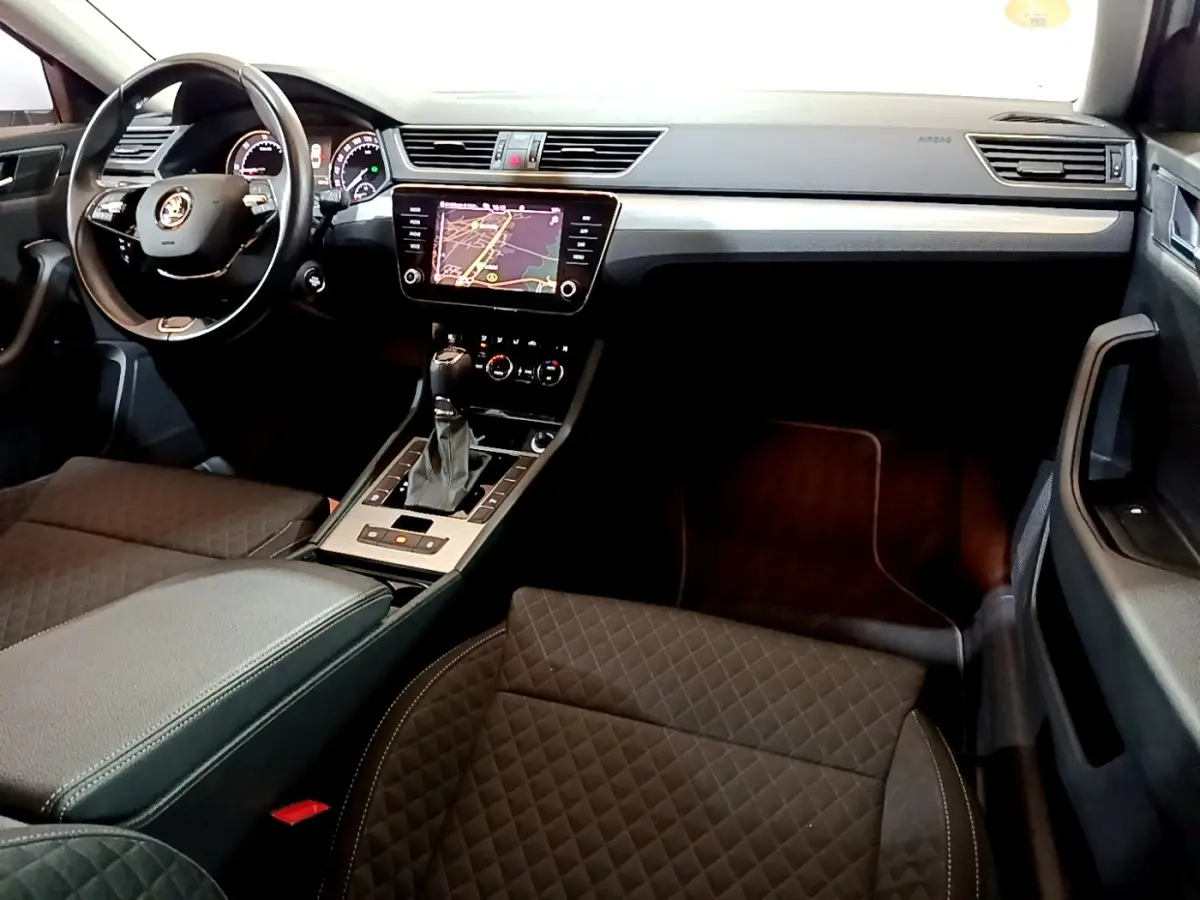 Vue intérieure côté conducteur de la Skoda Superb 2021, tableau de bord noir avec écran tactile et sièges en tissu matelassé.