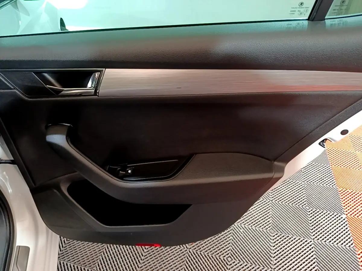 Vue rapprochée de la porte avant gauche blanche d'une Skoda Superb 2021 avec garniture noire et insert imitation bois.