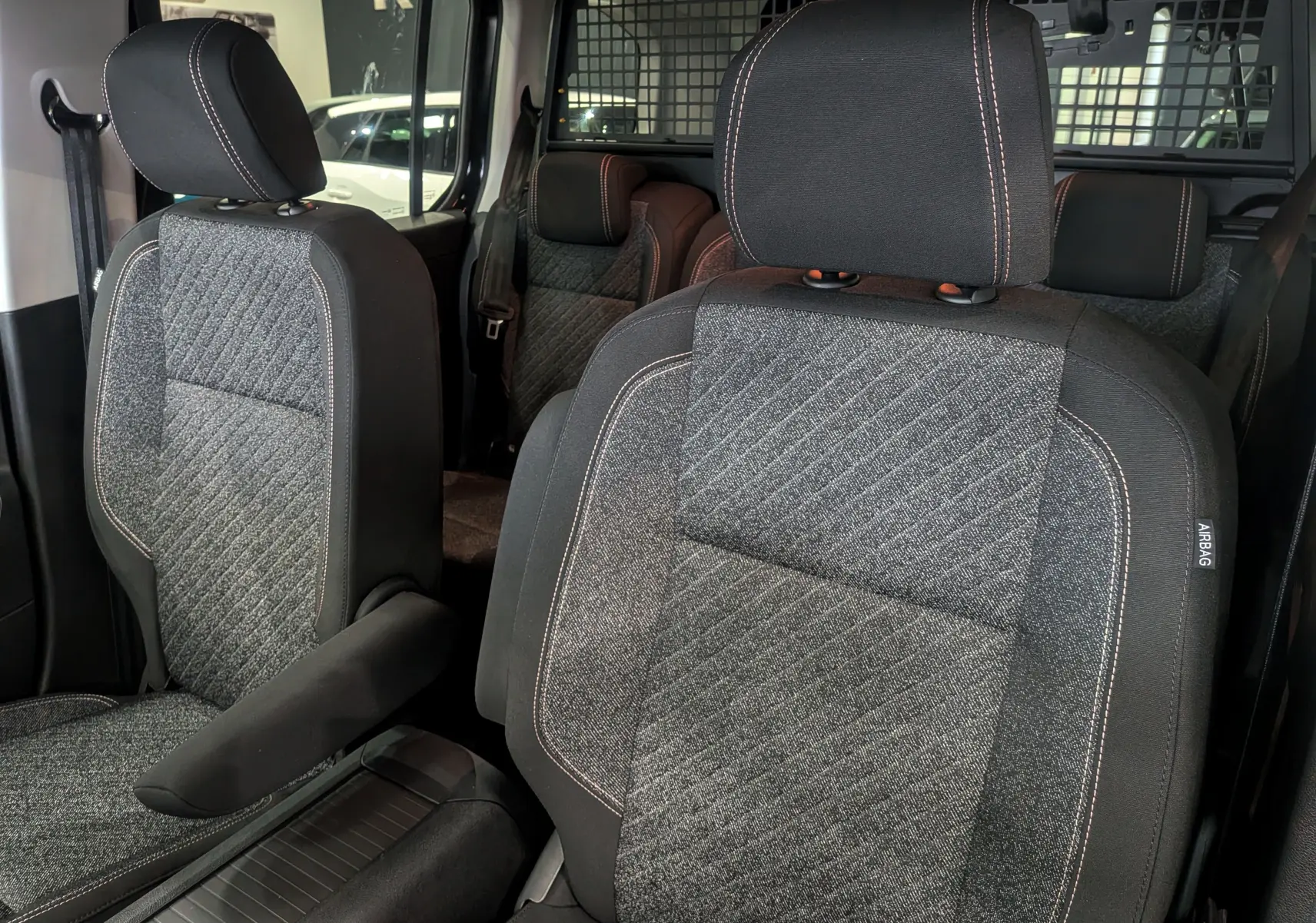 Gros plan sur les sièges avant en tissu gris et noir du Peugeot Rifter 2025, avec surpiqûres contrastantes et appuie-bras.