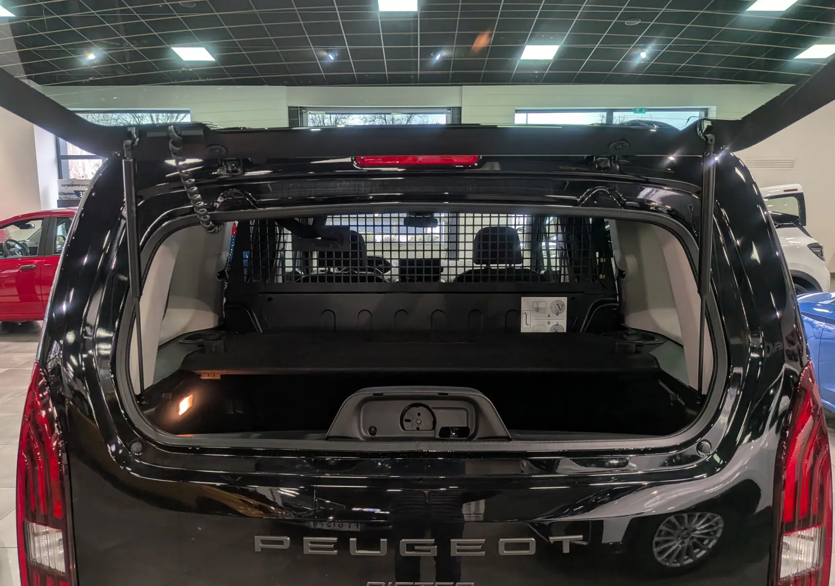Vue arrière du Peugeot Rifter noir 2025 avec hayon ouvert, montrant le coffre et la grille de séparation intérieure.