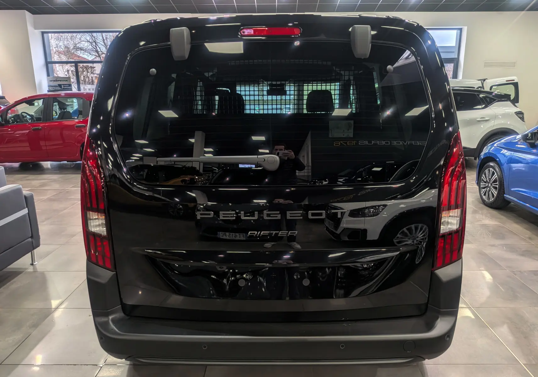 Vue arrière d'un Peugeot Rifter noir 2025 dans un showroom, avec feux arrière verticaux et vitre teintée.