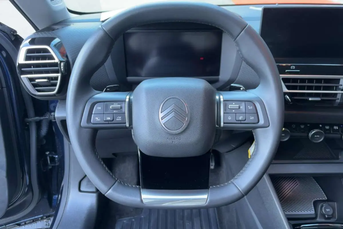Vue frontale du volant cuir multifonctions de la Citroën C4 hybride bleu eclipse, avec tableau de bord numérique et écran tactile.