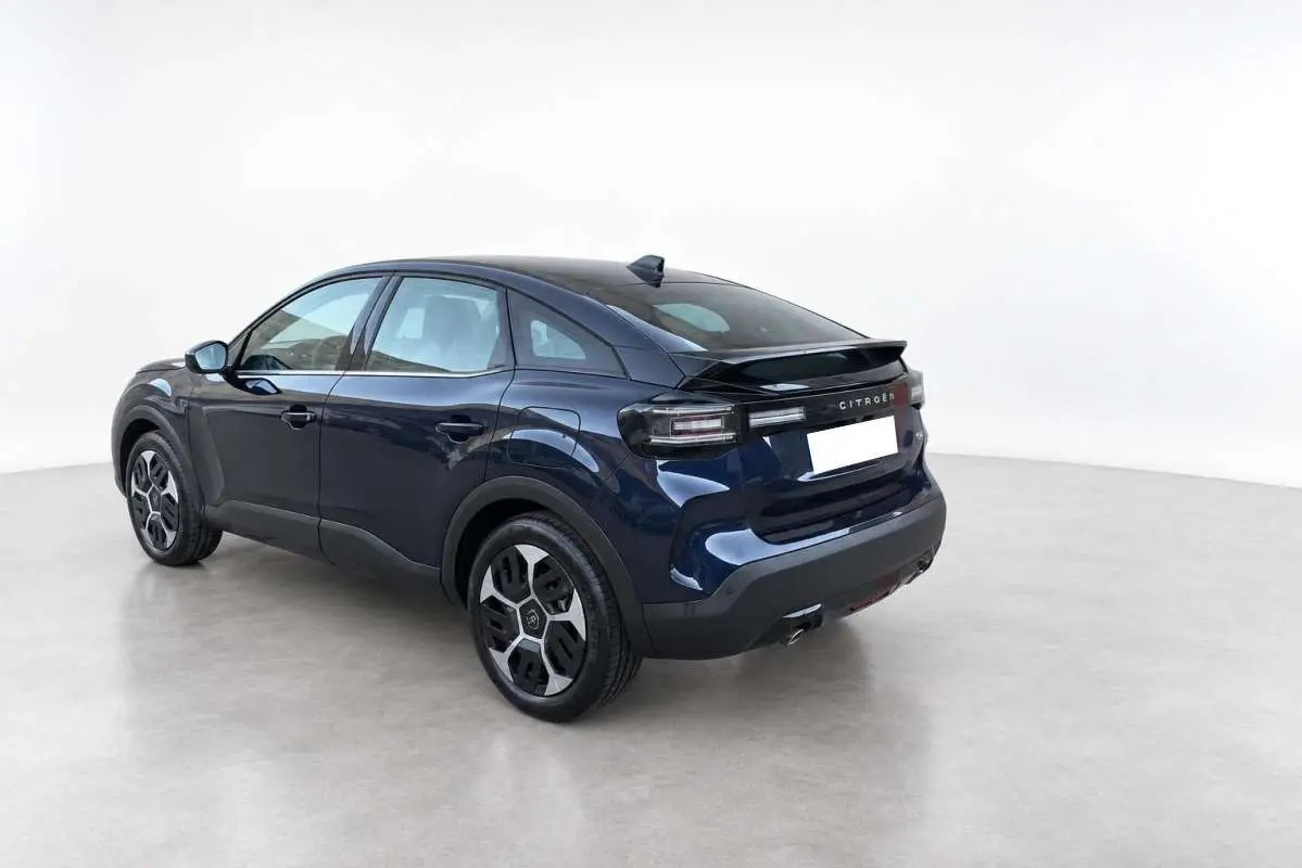 Vue 3/4 arrière droite d'une Citroën C4 hybride 2025 bleu eclipse avec toit noir et feux arrière LED distinctifs.