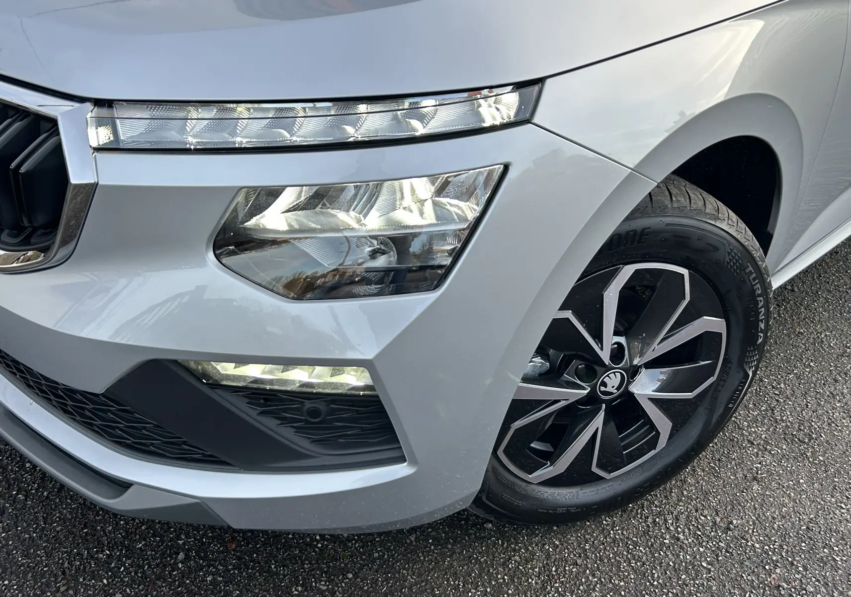 Gros plan sur l'avant droit gris argent métallisé du Skoda Kamiq 2025, mettant en valeur les phares LED et la jante noire à motifs géométriques.