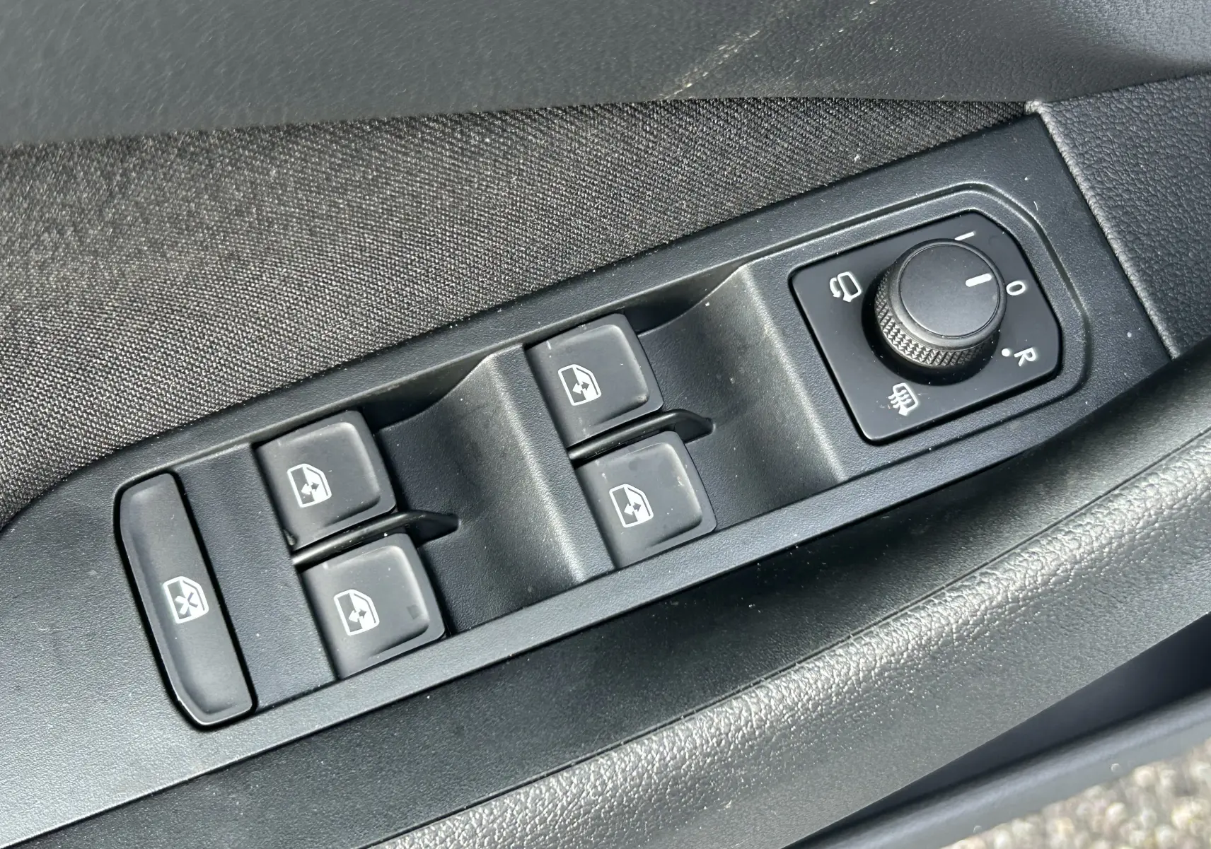 Gros plan sur les commandes de lève-vitres et réglage des rétroviseurs côté conducteur d’un Skoda Kamiq gris argent.