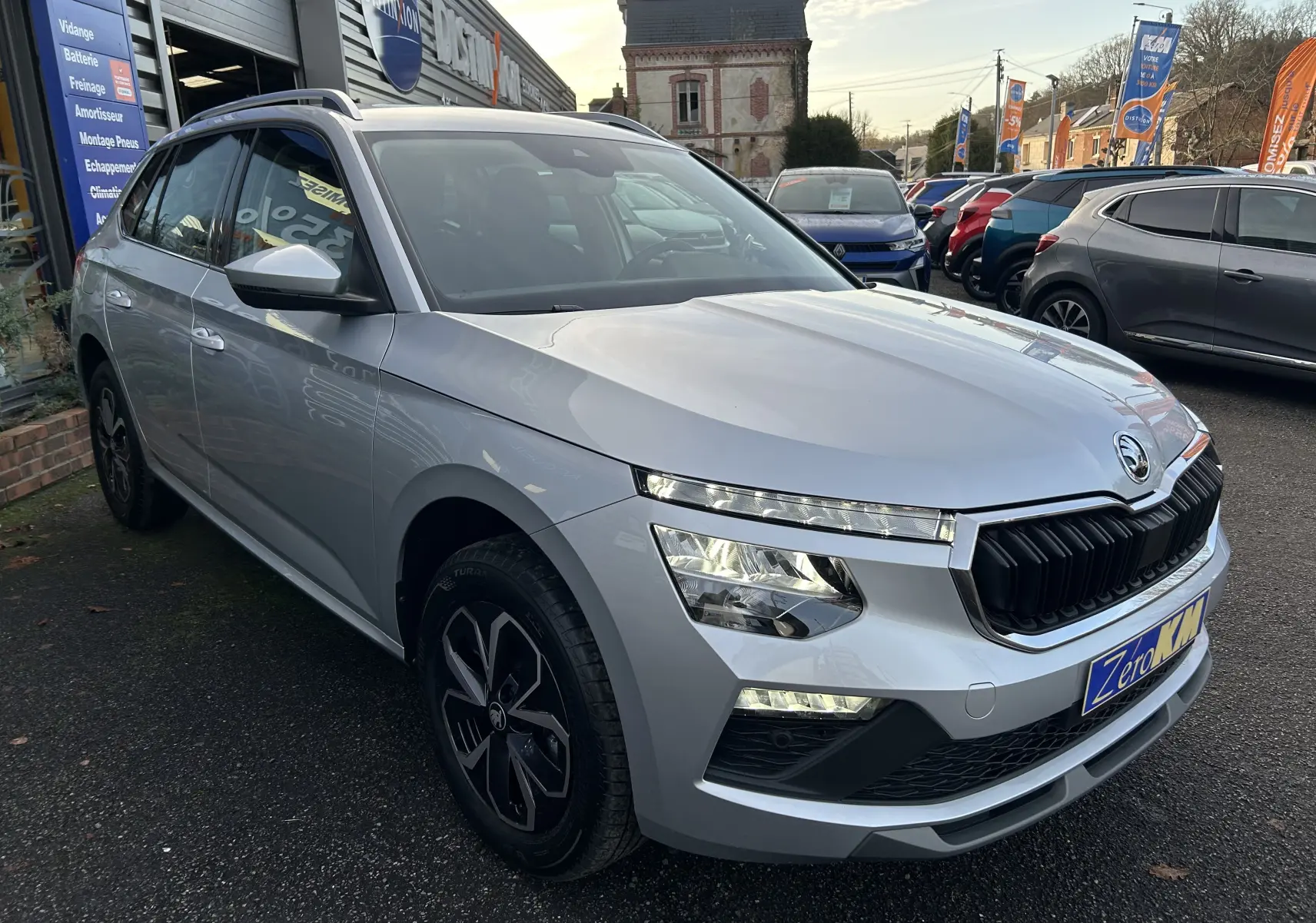 Vue 3/4 avant d'une Skoda Kamiq gris argent métal 2025, avec calandre noire et feux LED allumés.