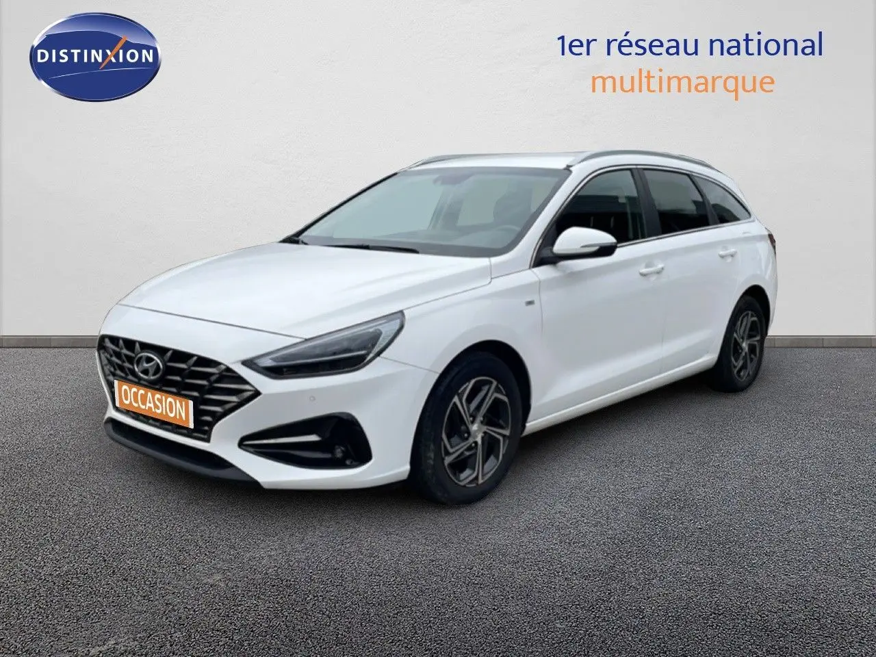Vue 3/4 avant droit d'une Hyundai i30 SW blanche Atlas avec calandre noire et jantes alliage distinctives.