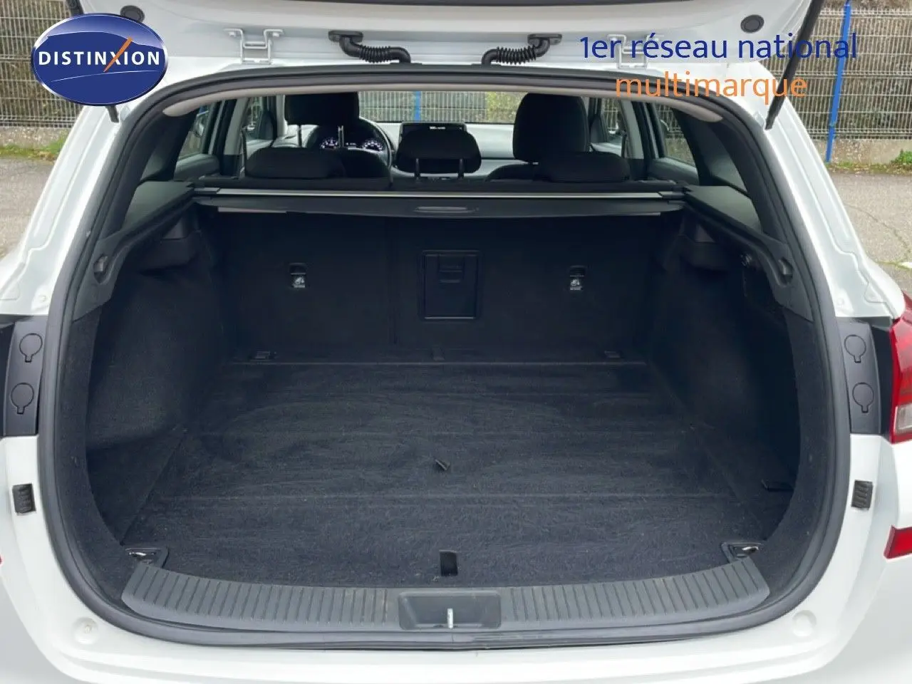 Coffre ouvert d'une Hyundai i30 SW blanc atlas, vue arrière montrant l'espace de chargement vide et la plage arrière.