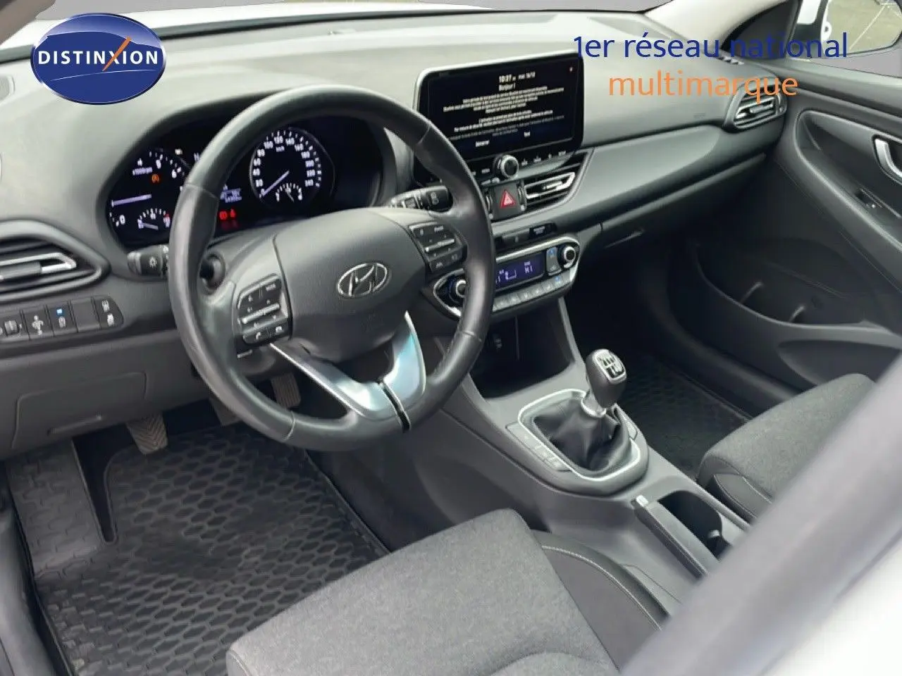 Vue intérieure côté conducteur de la Hyundai i30 SW 2023, tableau de bord moderne avec écran tactile et boîte manuelle.