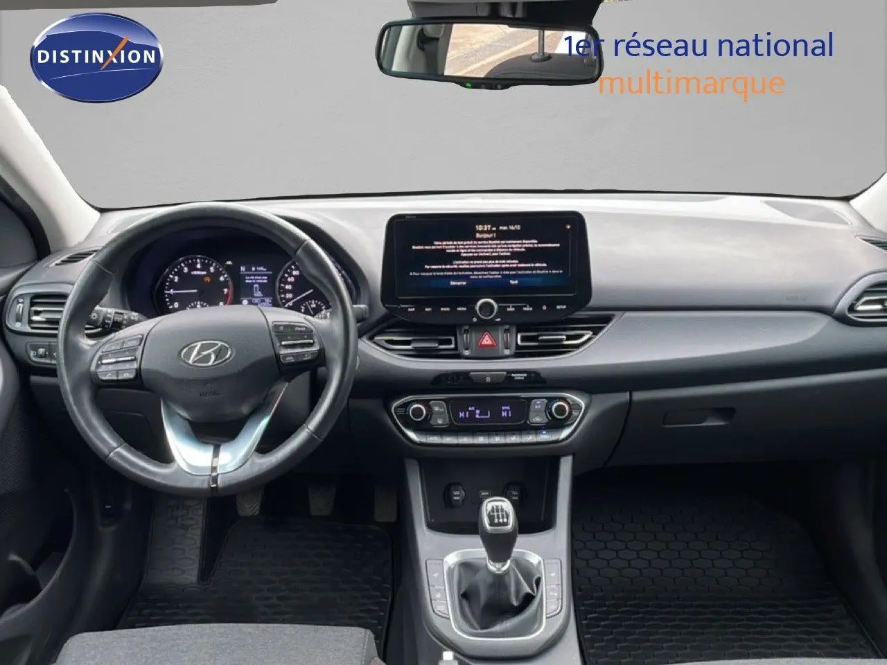 Vue intérieure frontale du tableau de bord et volant noir de la Hyundai i30 SW 2023 avec écran tactile et boîte manuelle.