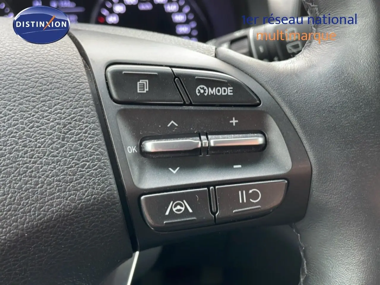 Gros plan sur les commandes au volant noir du Hyundai i30 SW 2023, avec boutons de mode et régulateur de vitesse.