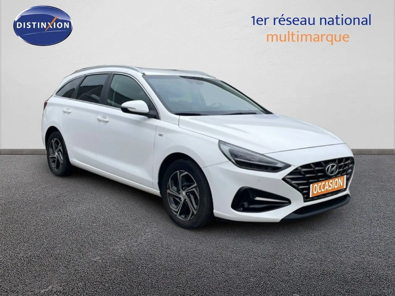 Vue 3/4 avant droit d'une Hyundai i30 SW blanche avec calandre noire et jantes alliage distinctives.