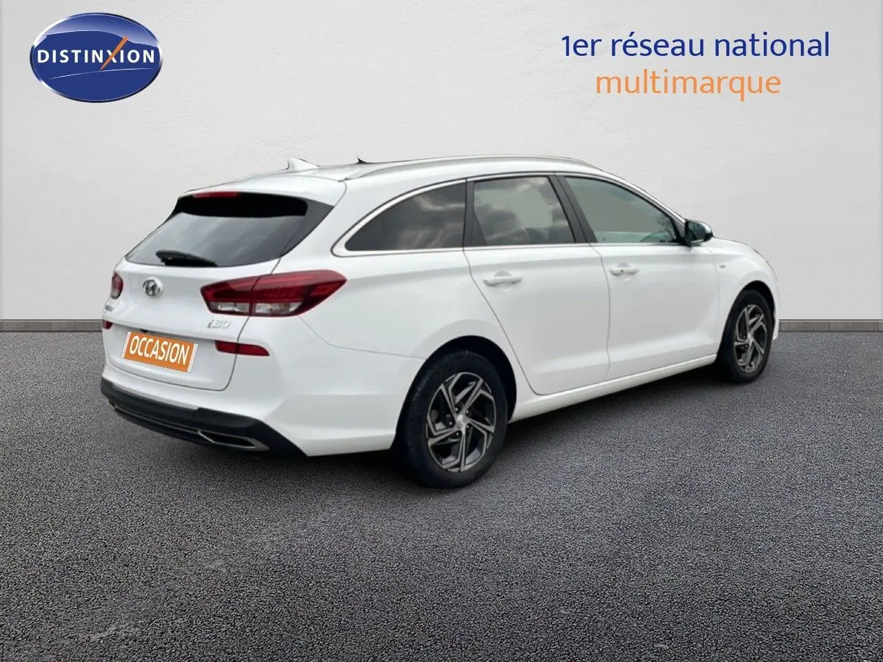 Vue 3/4 arrière droite d'une Hyundai i30 SW blanche Atlas avec jantes alliage et vitres teintées.