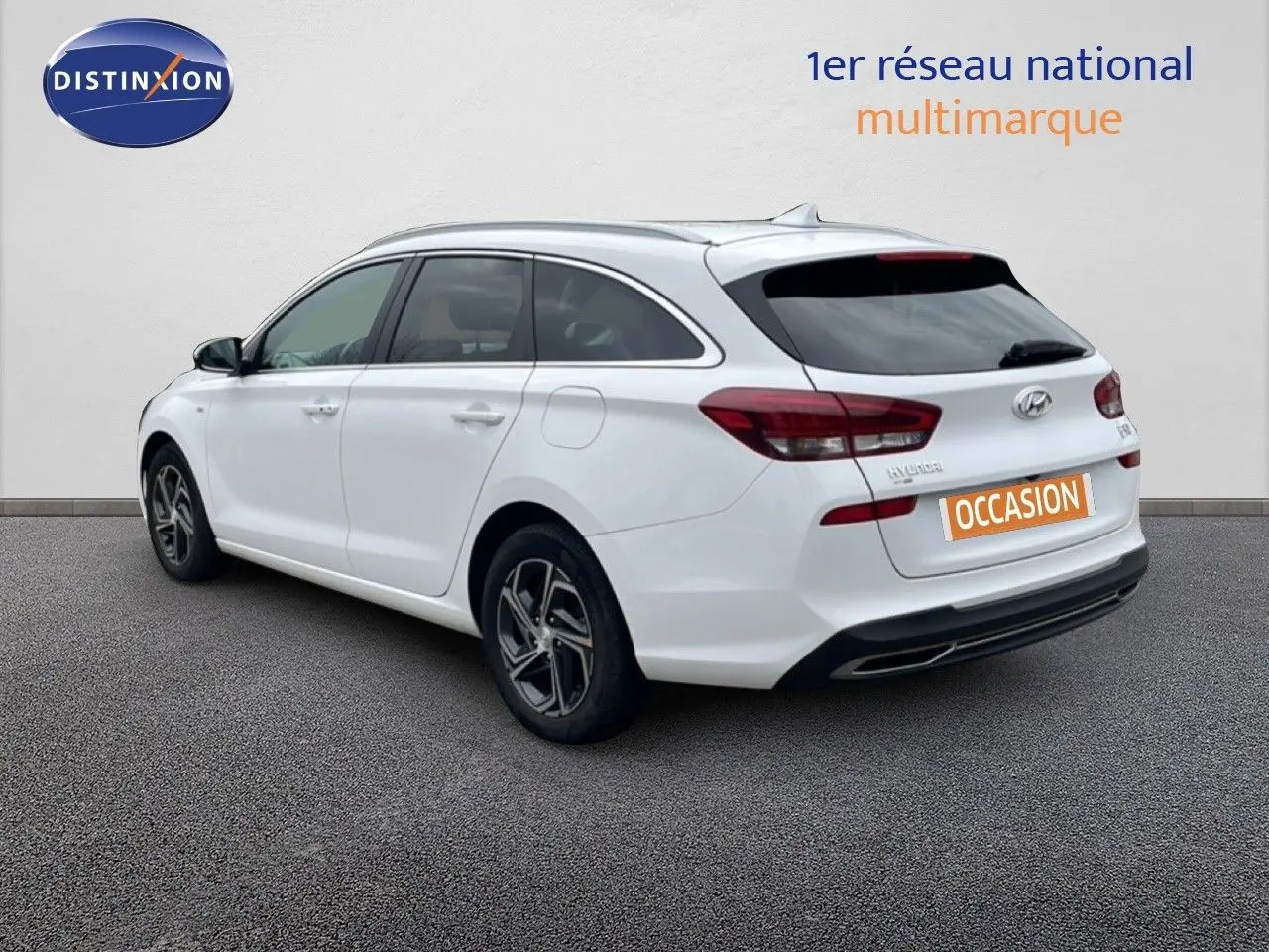 Vue 3/4 arrière droite d'une Hyundai i30 SW blanche Atlas avec jantes alliage et vitres teintées.