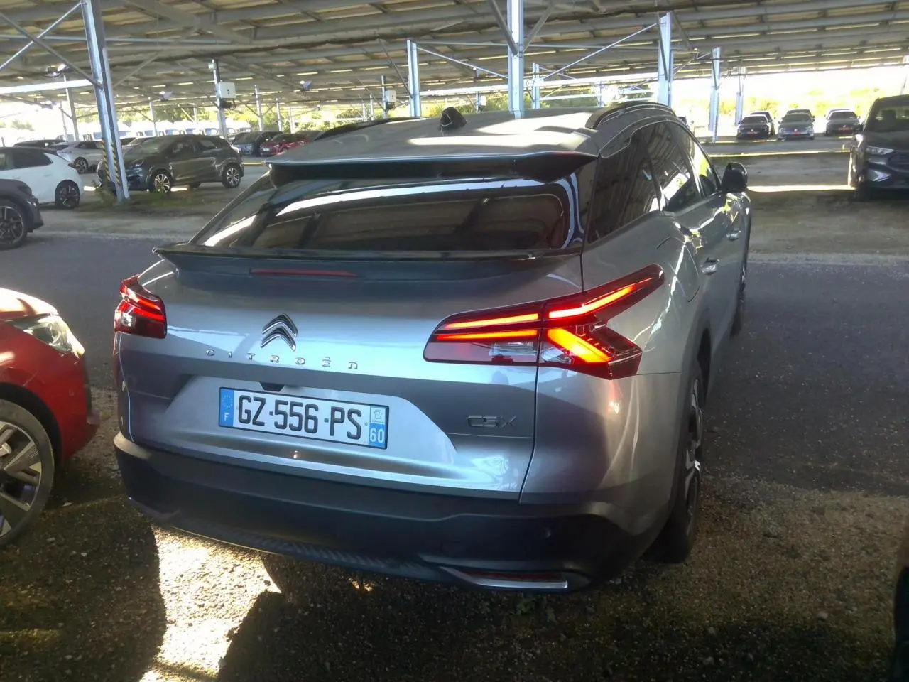 Vue 3/4 arrière d'une Citroën C5 X 2024 gris foncé avec feux arrière allumés, stationnée sous abri.