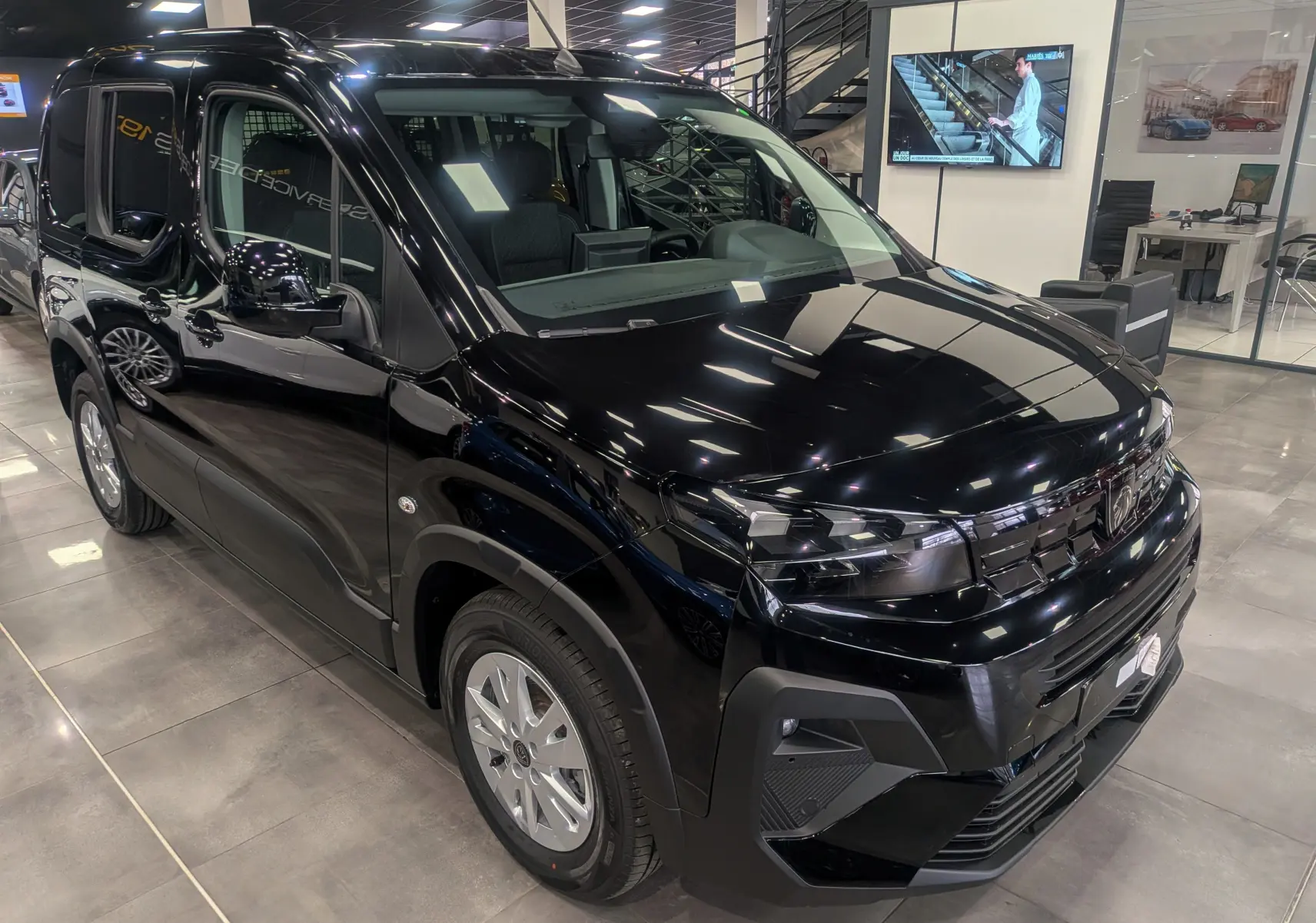 Peugeot Rifter noir vue 3/4 avant droit en showroom, avec calandre et optiques modernes visibles.