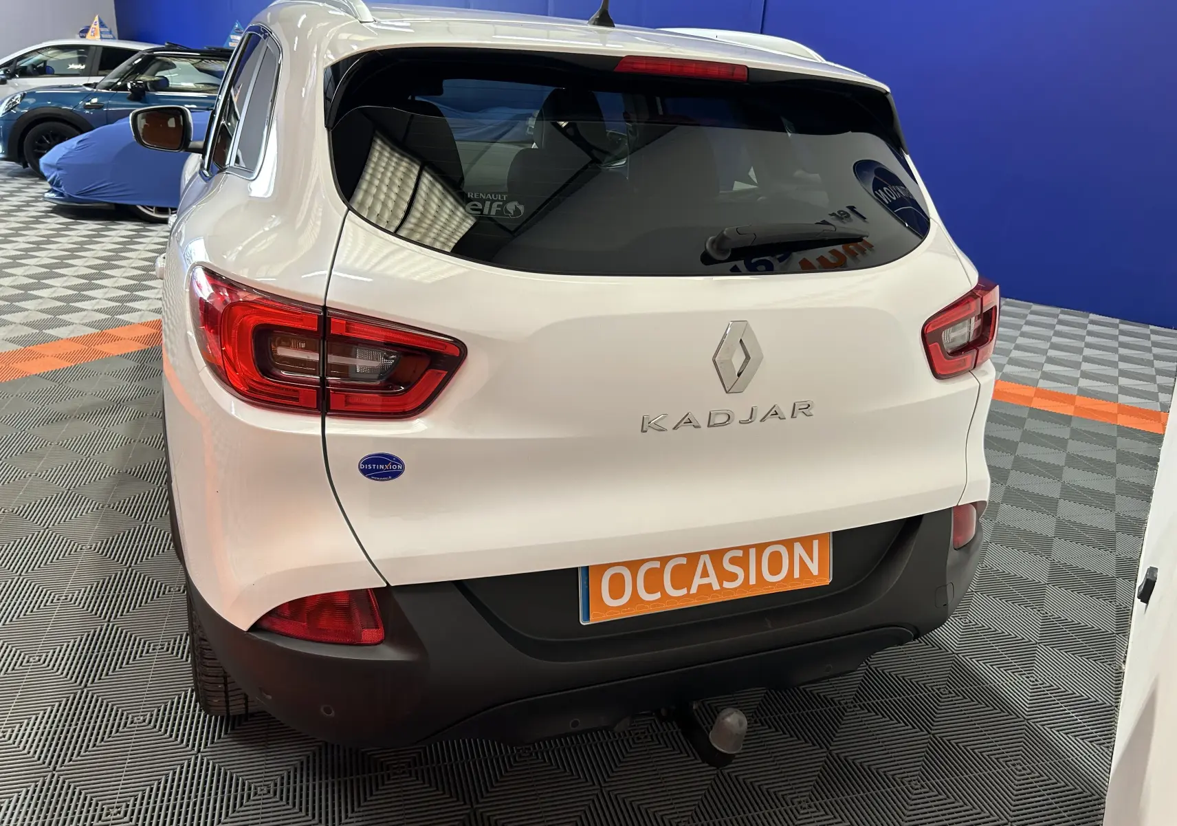 Vue arrière d'un Renault Kadjar blanc avec attelage et plaque orange "OCCASION" dans un showroom.