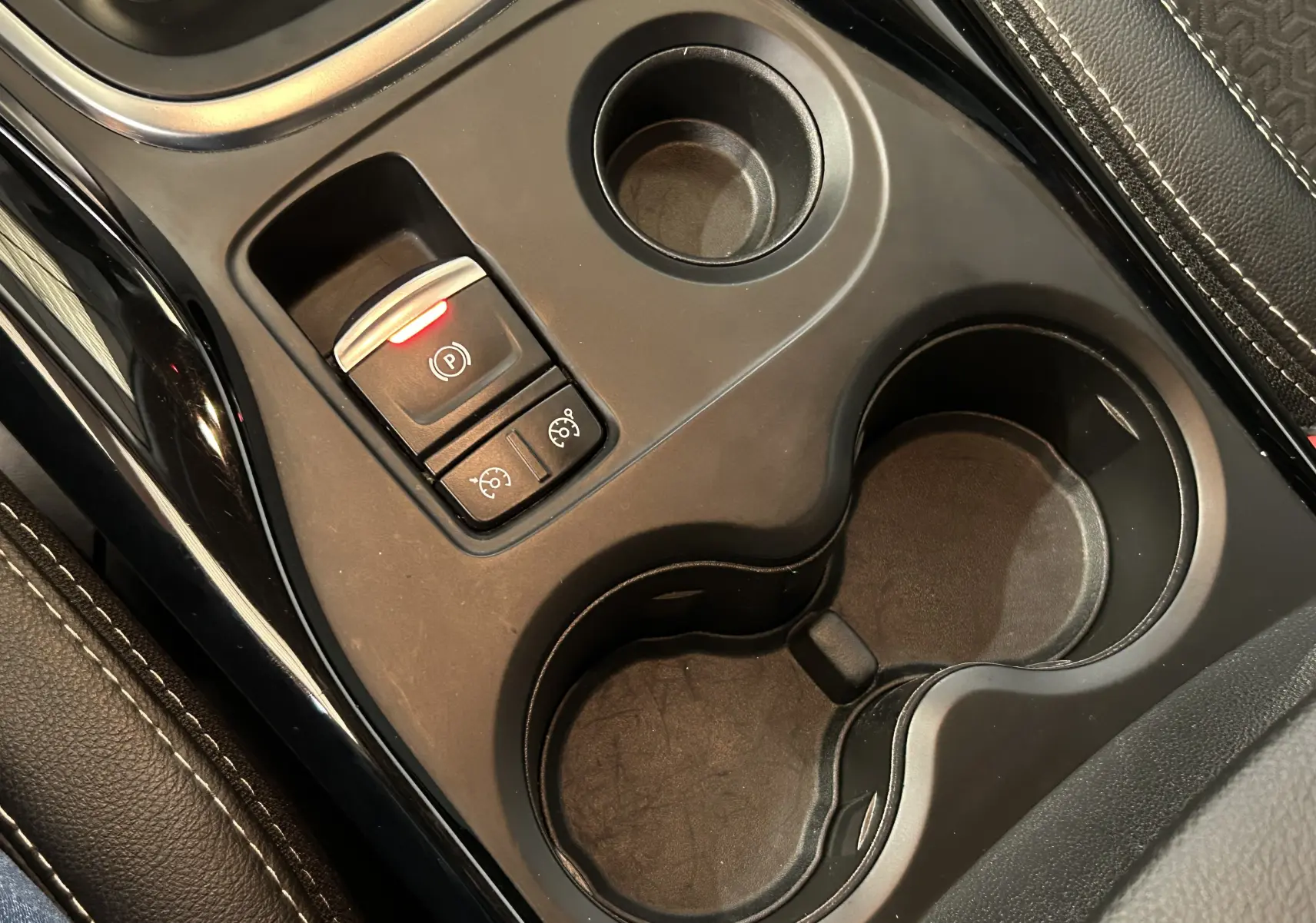 Gros plan sur la console centrale noire du Renault Kadjar 2018 avec porte-gobelets et bouton de frein à main électrique allumé.