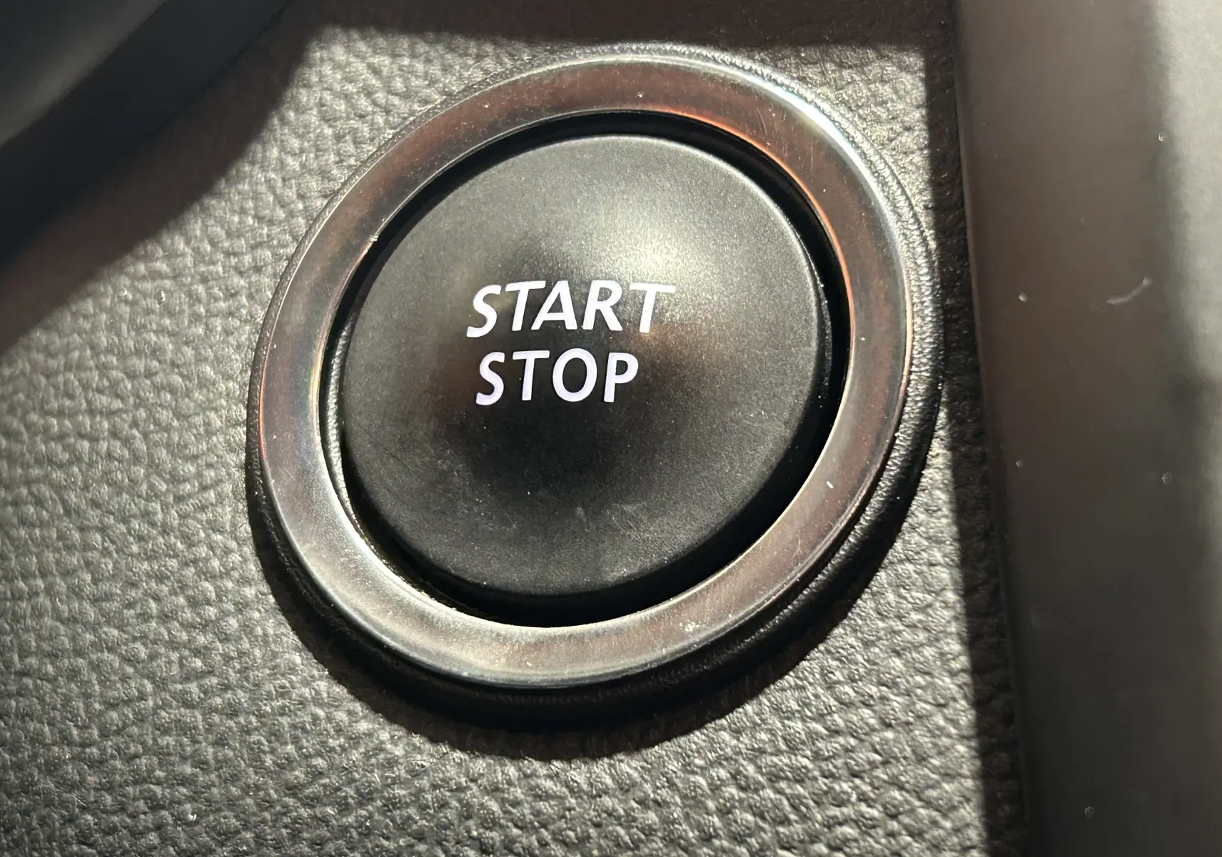 Gros plan sur le bouton Start Stop noir entouré d’un anneau chromé dans l’habitacle du Renault Kadjar blanc.