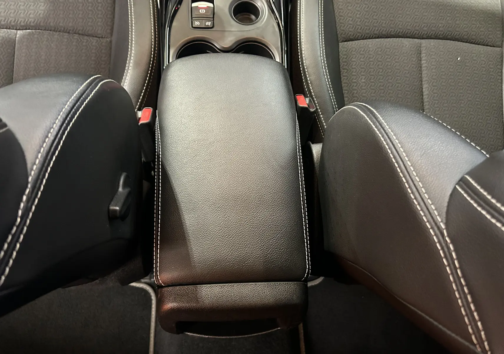 Vue intérieure centrée sur l'accoudoir noir en cuir avec surpiqûres blanches entre les sièges avant gris du Renault Kadjar.