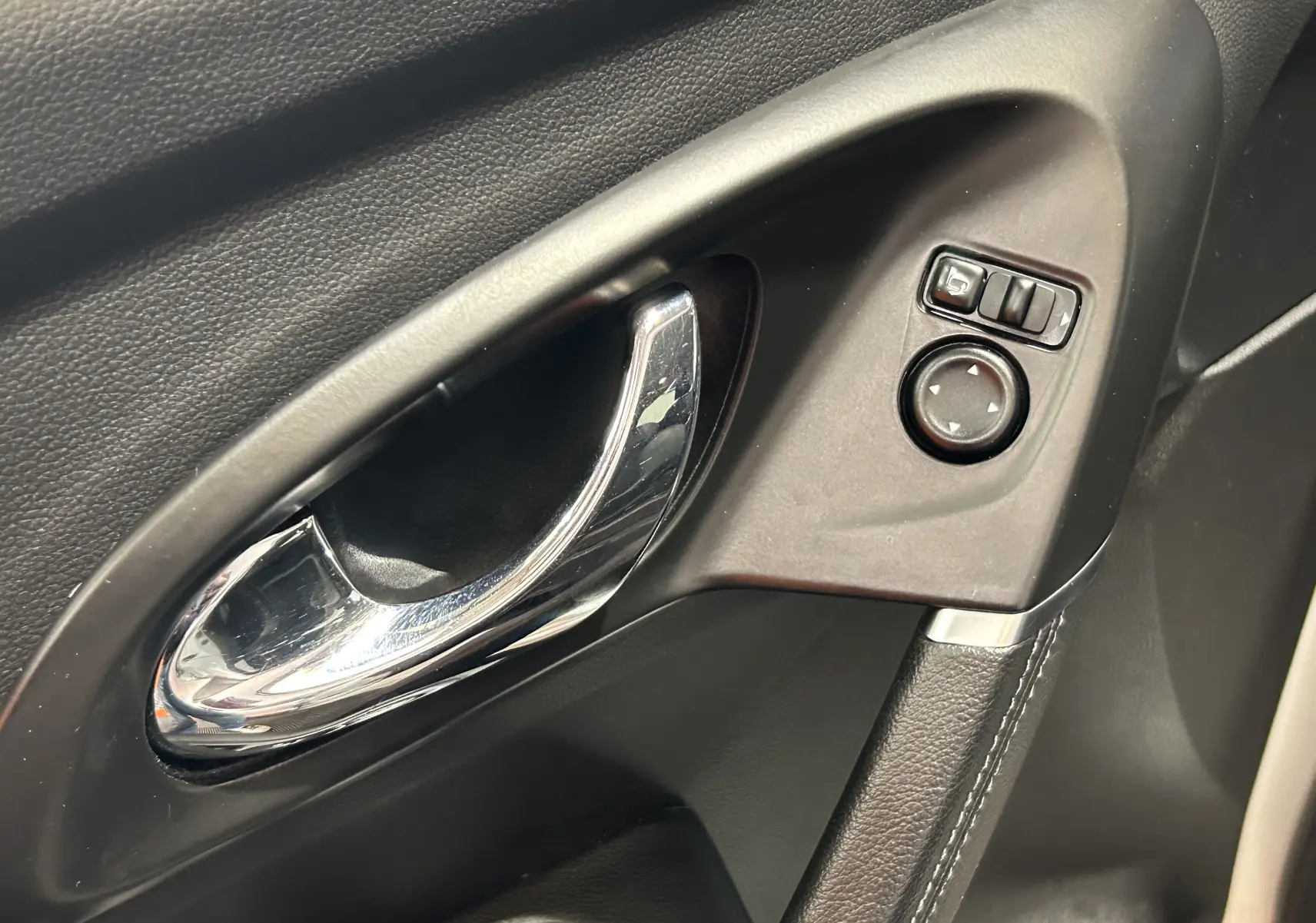 Poignée de porte intérieure côté gauche en plastique noir avec commande de réglage des rétroviseurs sur Renault Kadjar blanc.